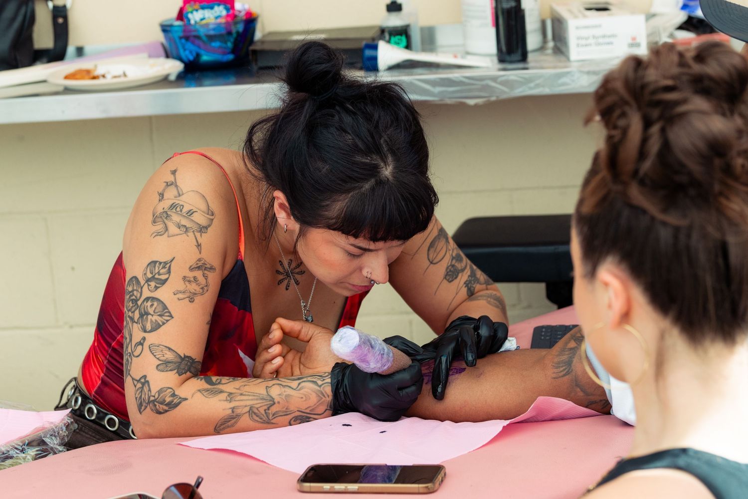 Close-up of a tattooed artist focused on inking a detailed tattoo on a client's arm.