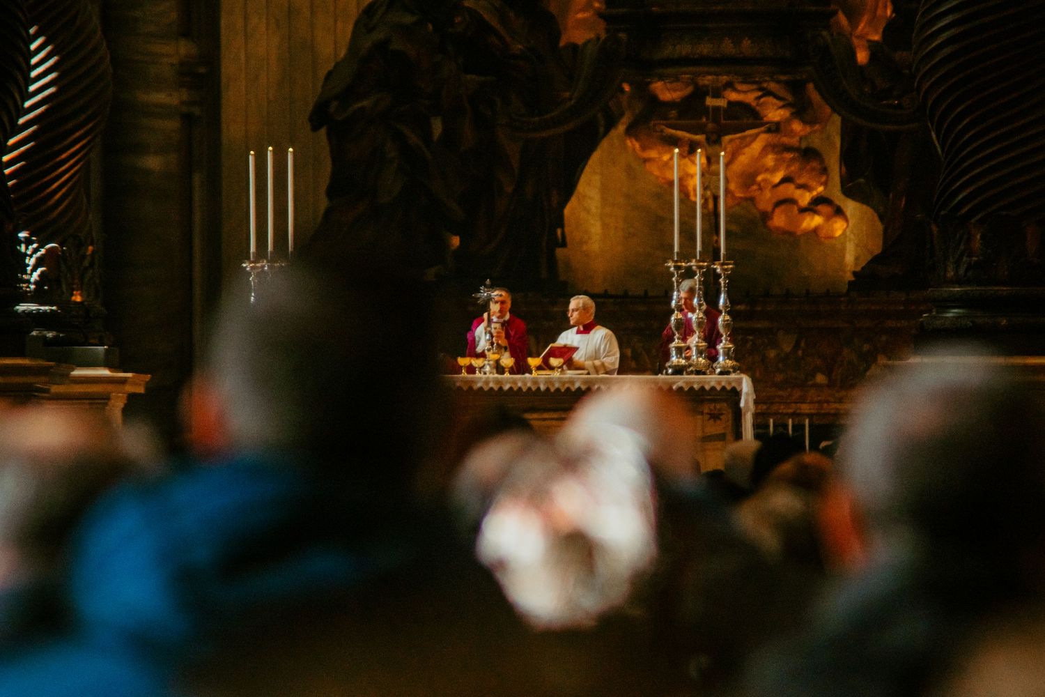 Catholic priests celebrate Mass at an ornate altar inside a historic church with congregation members in foreground.