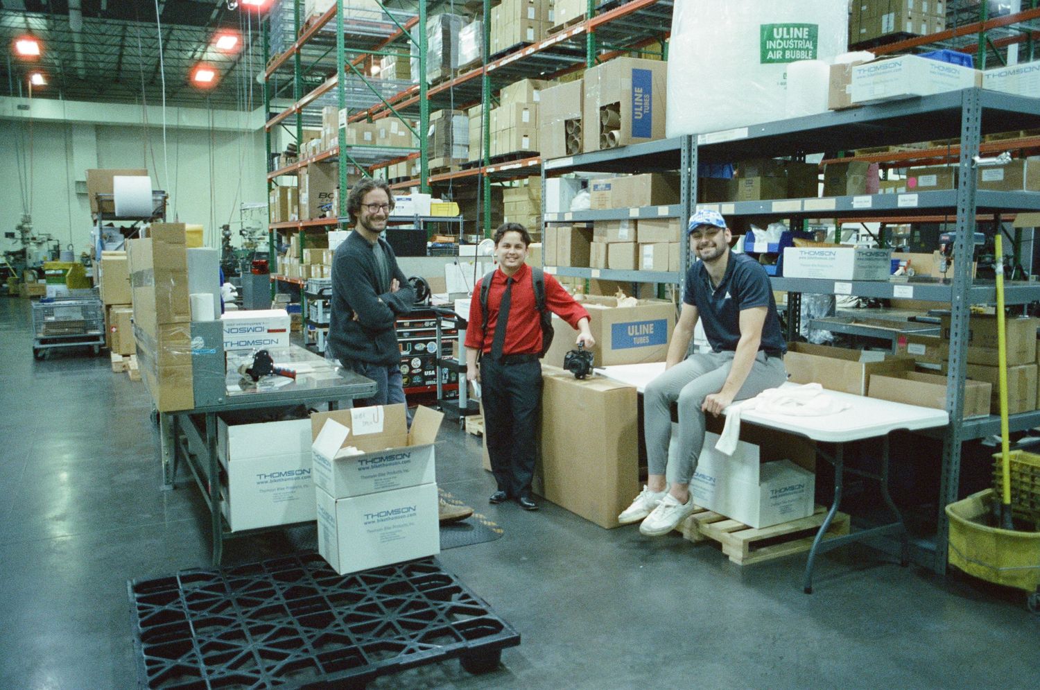 Three workers posing in a large warehouse surrounded by boxes and shelving.