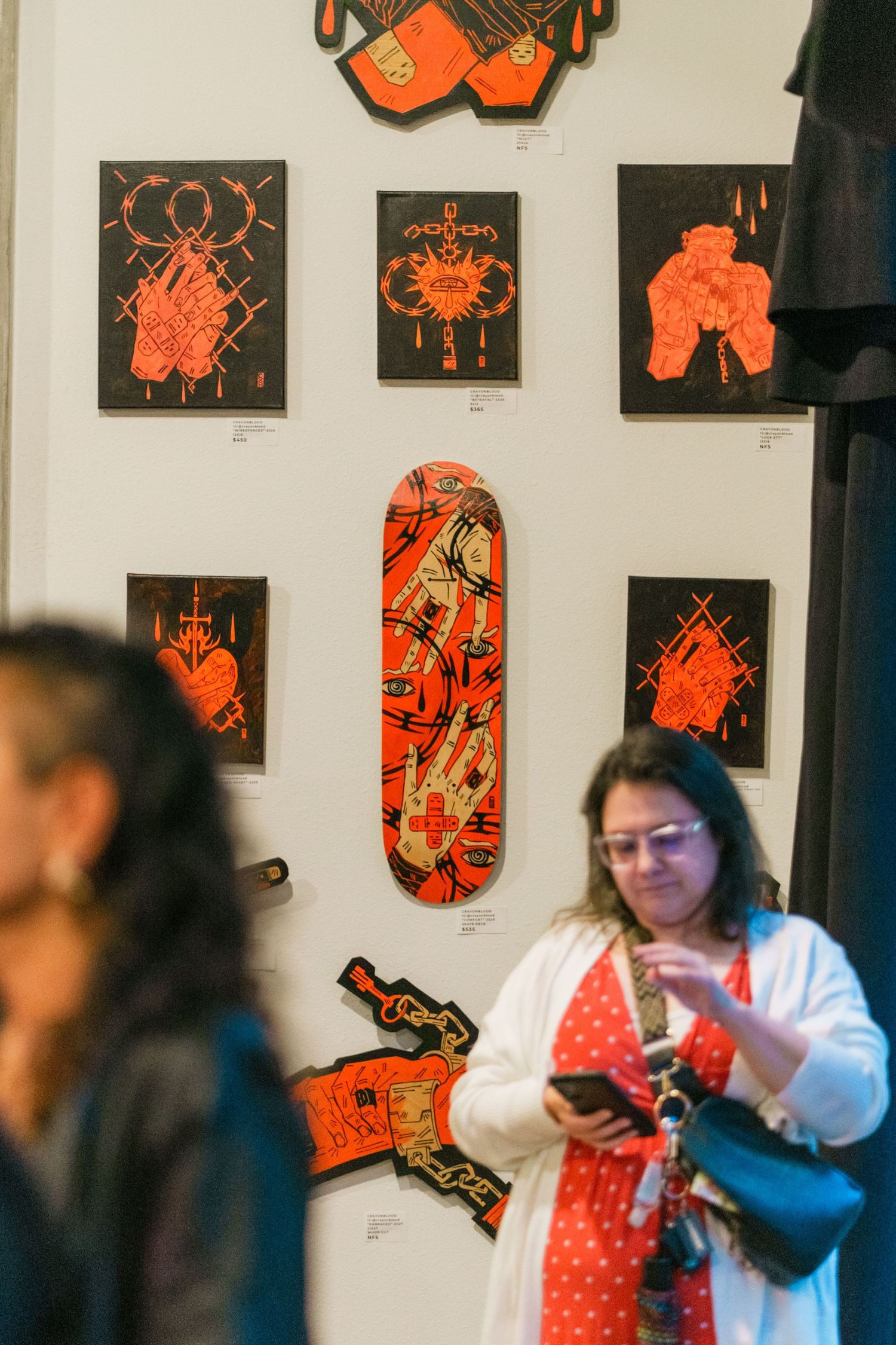 Woman in red dress browsing orange and black artwork and decorated skateboards at an art gallery show.