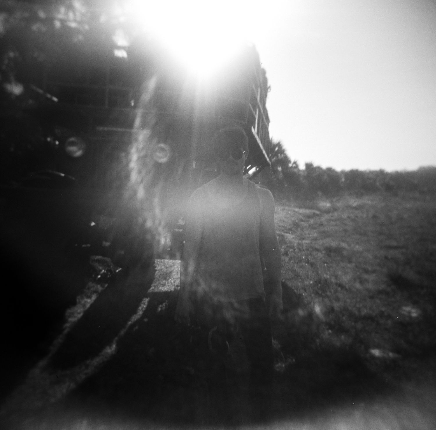 Black and white artistic photo of a motorcycle with dramatic sun flare on open grassy field.