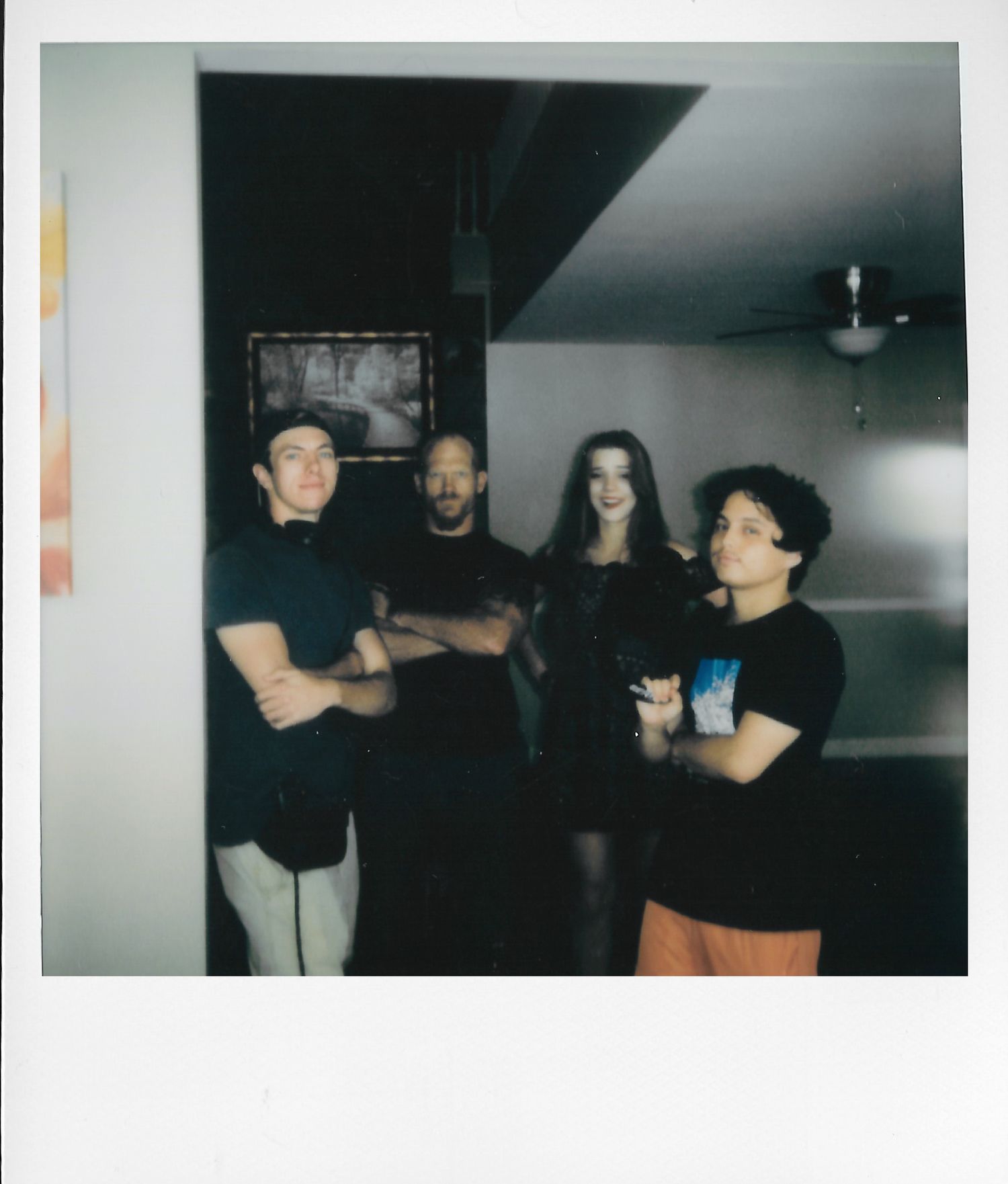 Four young adults posing together in a dimly lit room, captured in a retro Polaroid-style photograph.