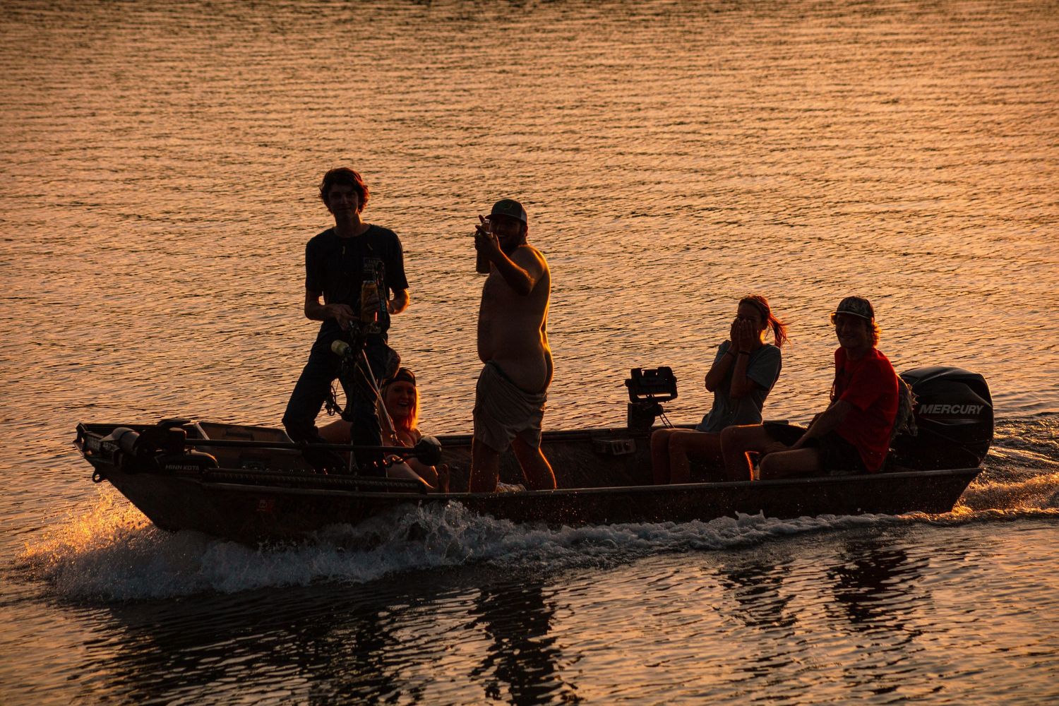 Silhouettes of four people riding a motorboat on golden water at sunset.