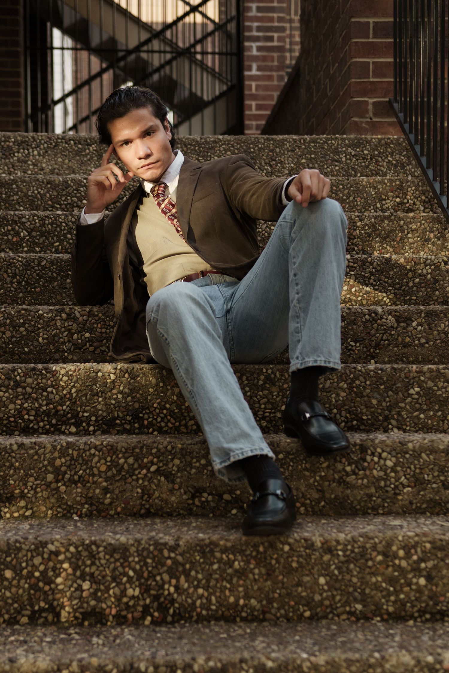 Vintage-styled portrait of a young man in a brown blazer sitting relaxed on outdoor stone steps, Austin lifestyle photography.