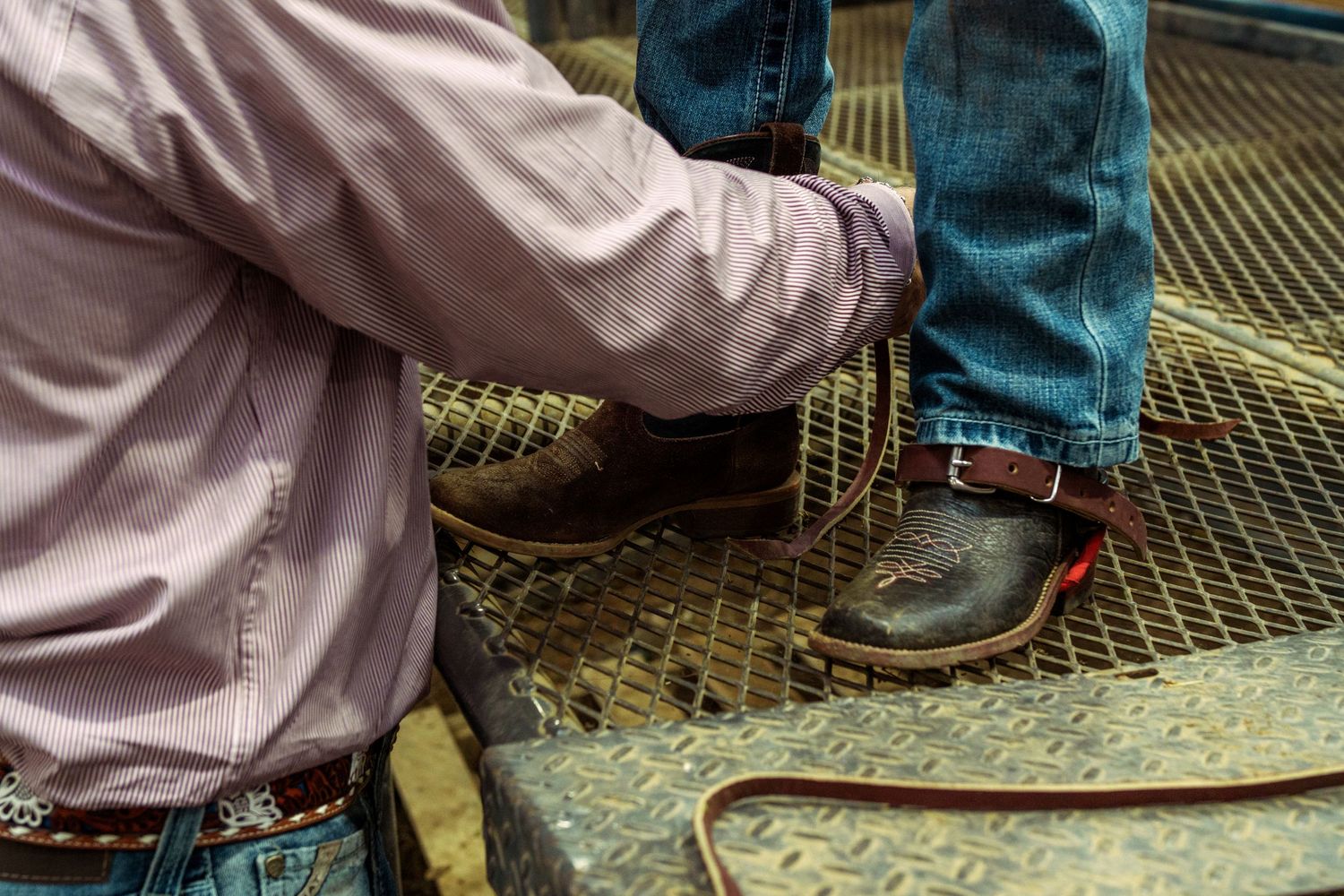 Close-up of two people wearing cowboy boots and jeans standing on a metal grate at a rodeo event.