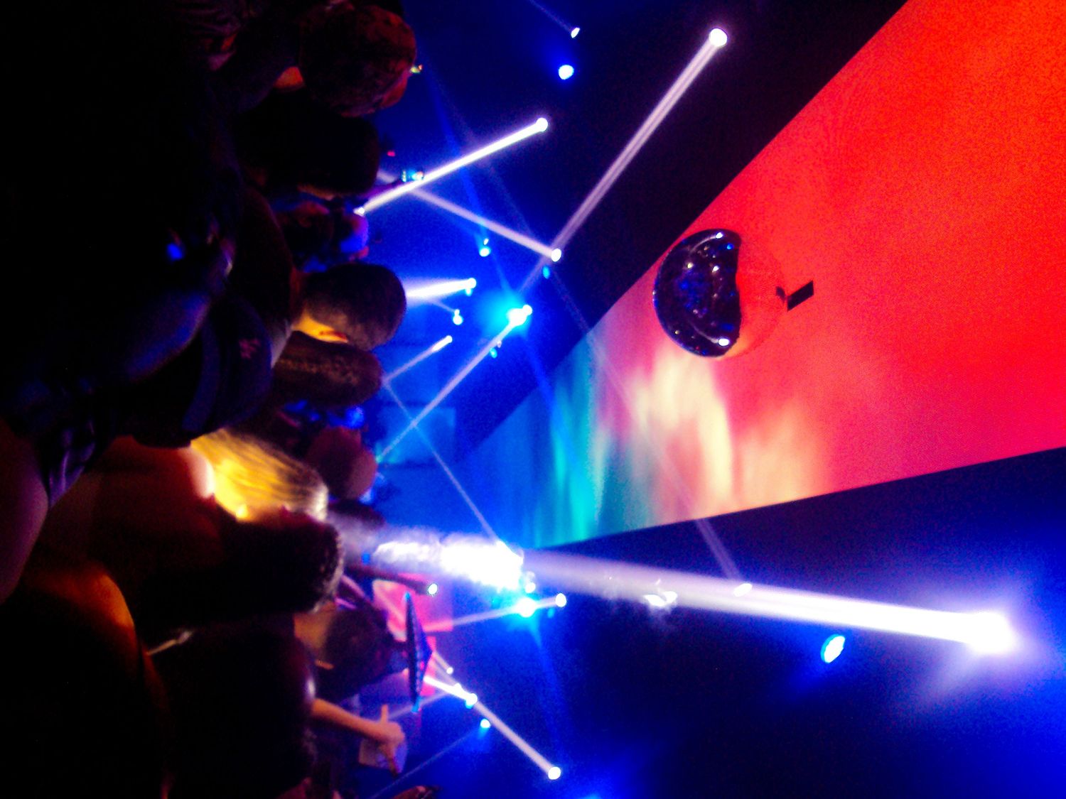 Colorful laser light show at a concert with blue beams and vibrant red and blue projection screen in dark venue.