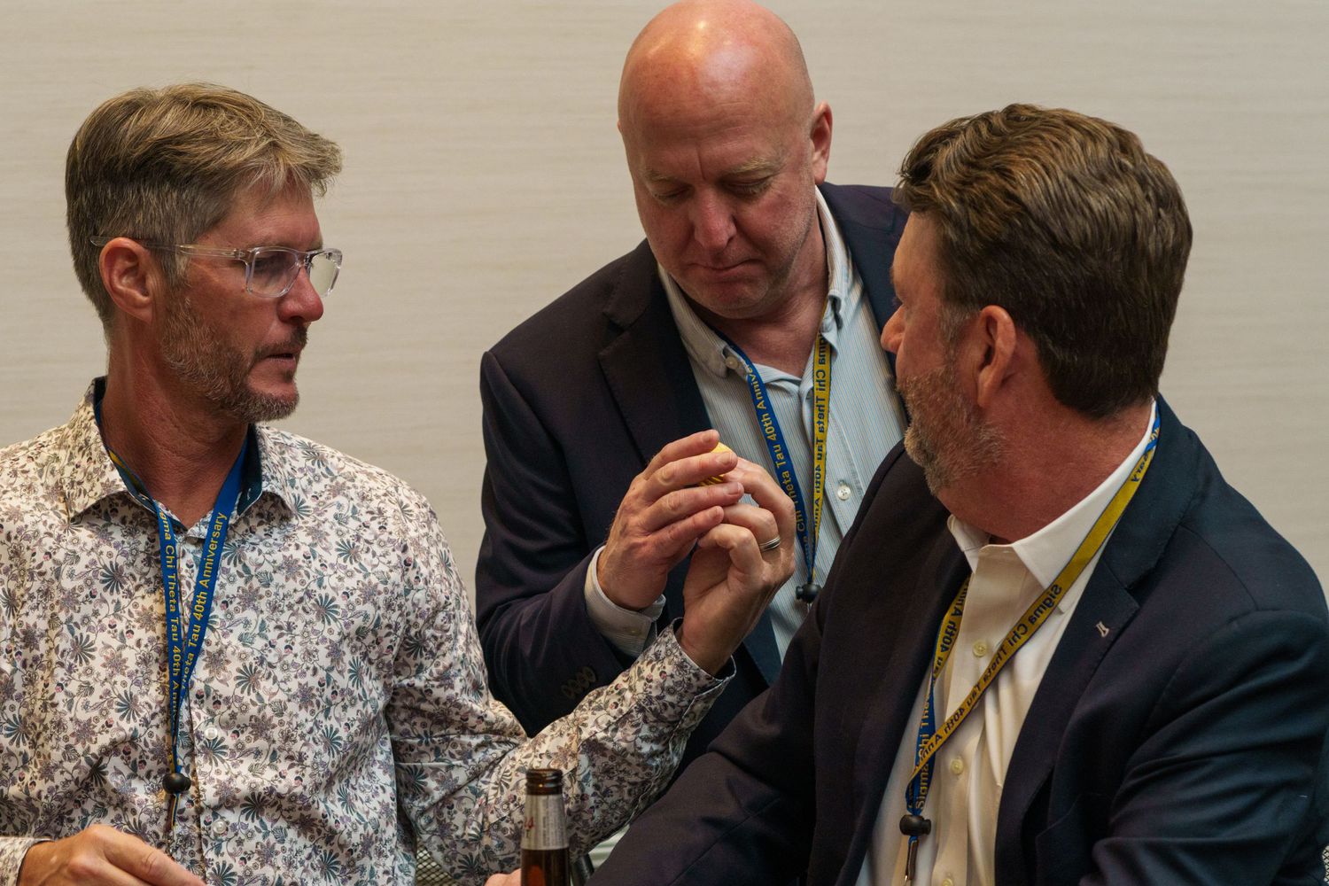 Three professional men in business casual attire engage in conversation at a conference event, wearing lanyards.