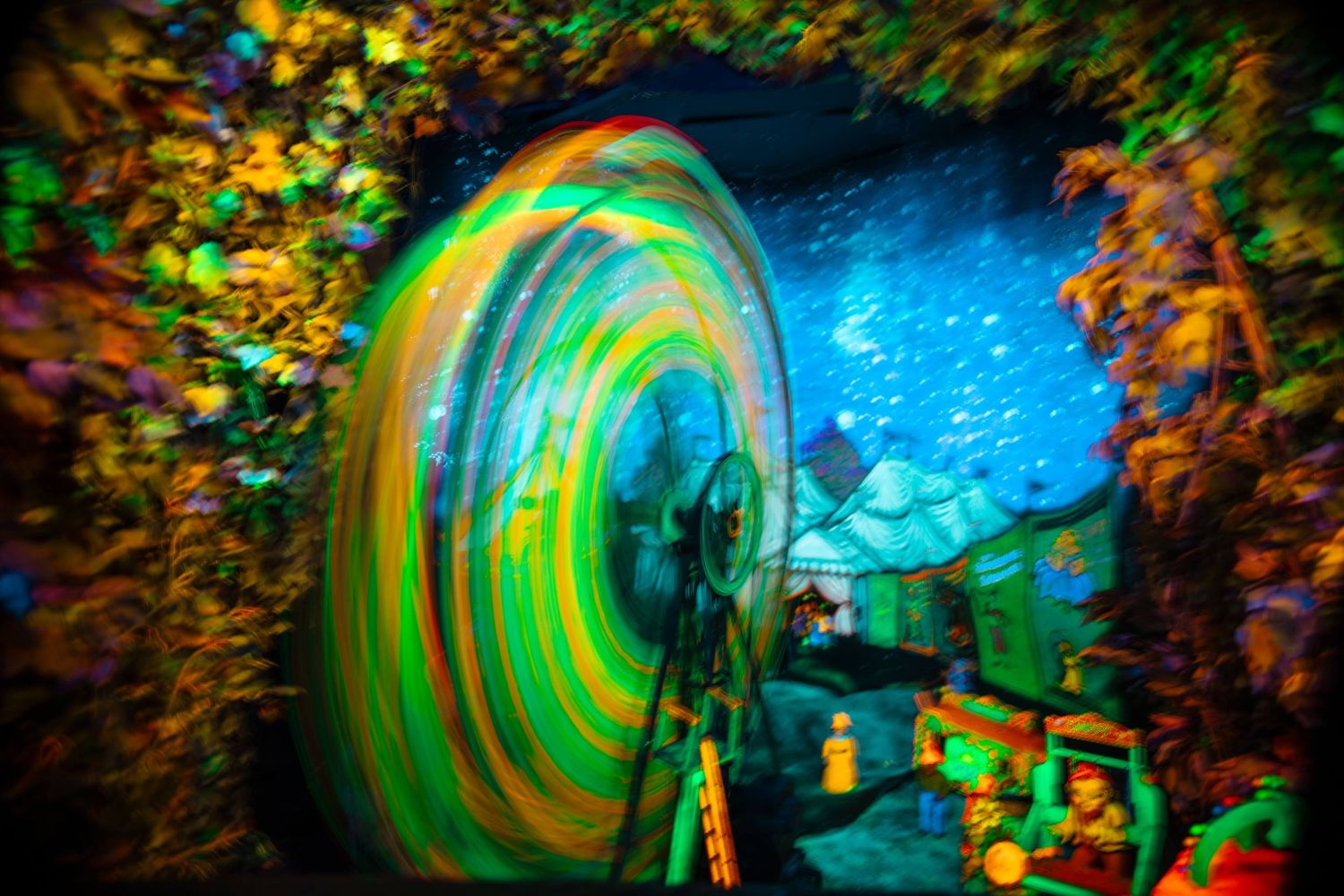 Colorful spinning tunnel illusion with vibrant green and yellow swirls in a dark immersive attraction exhibit.