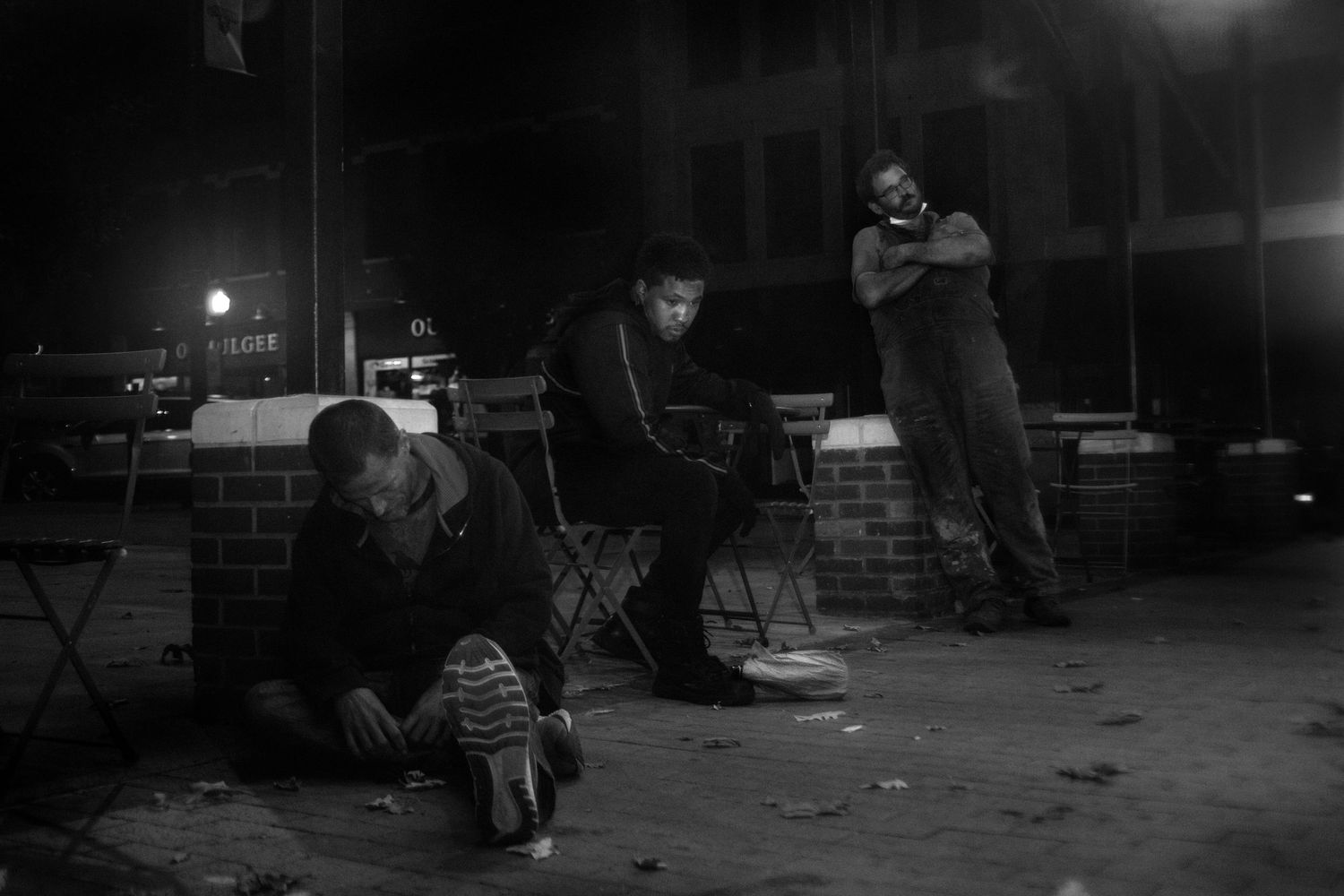 Black and white photo of three men gathered outside at night near a brick wall.