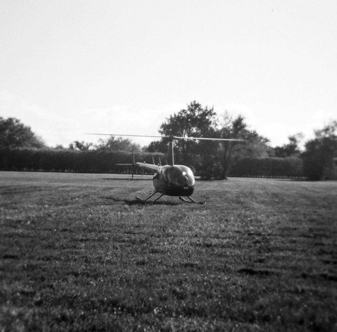 A small helicopter rests on a grass field with trees in the background, black and white photo.