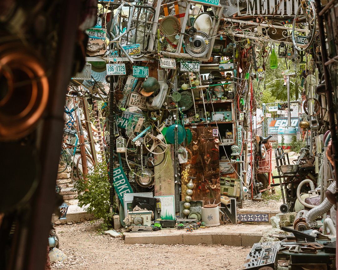 Eclectic outdoor art installation with vintage license plates, signs, and salvaged metal objects creating a unique sculptural environment.