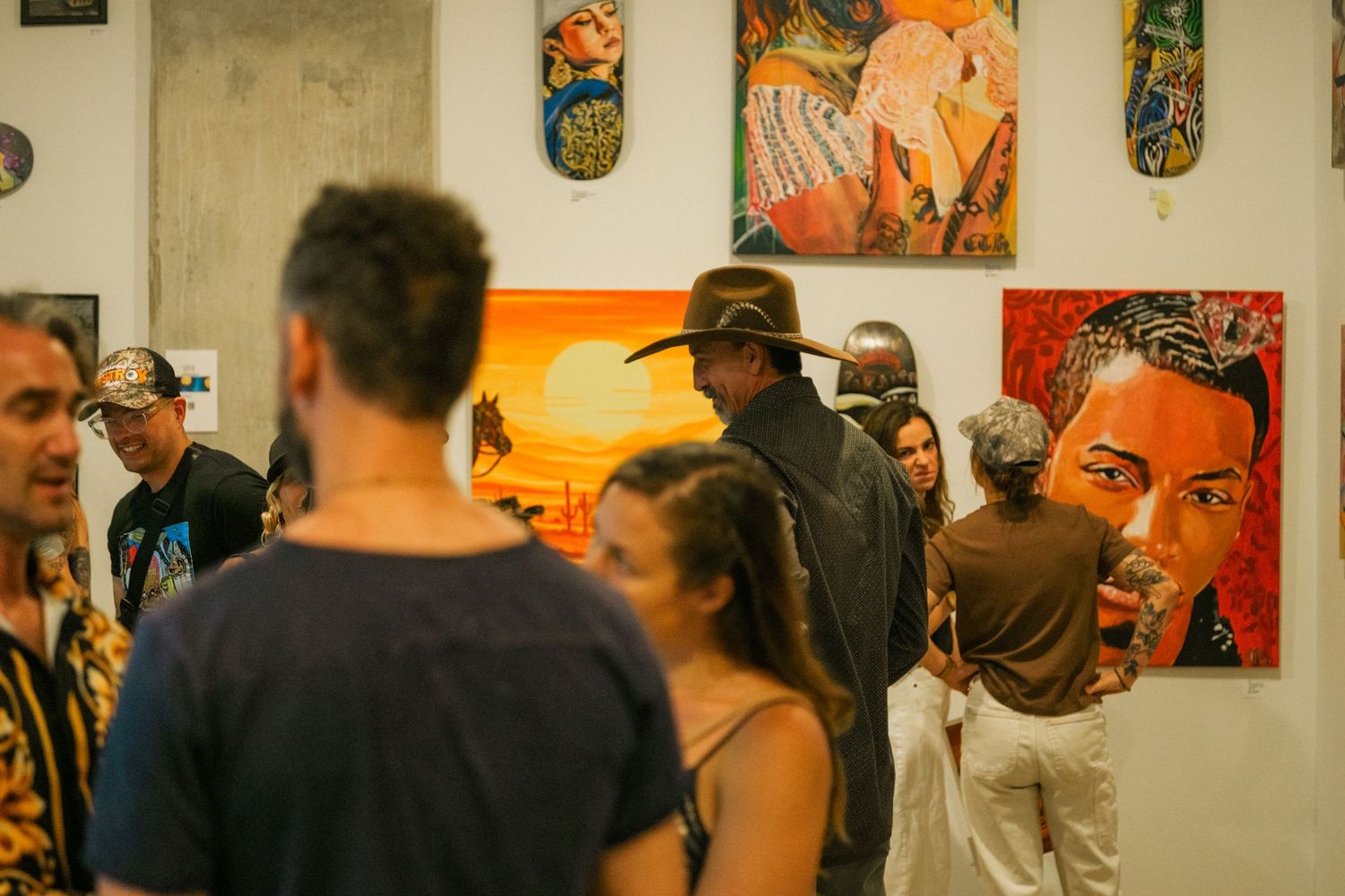 Crowd of art enthusiasts gather at a vibrant street art gallery opening featuring portraits and desert landscapes.