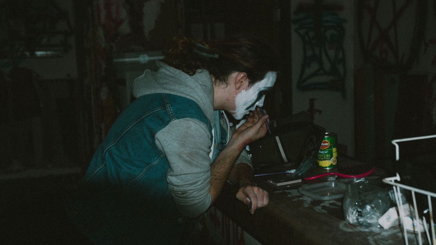 Person leaning over table in dimly lit room with shaving cream on face.