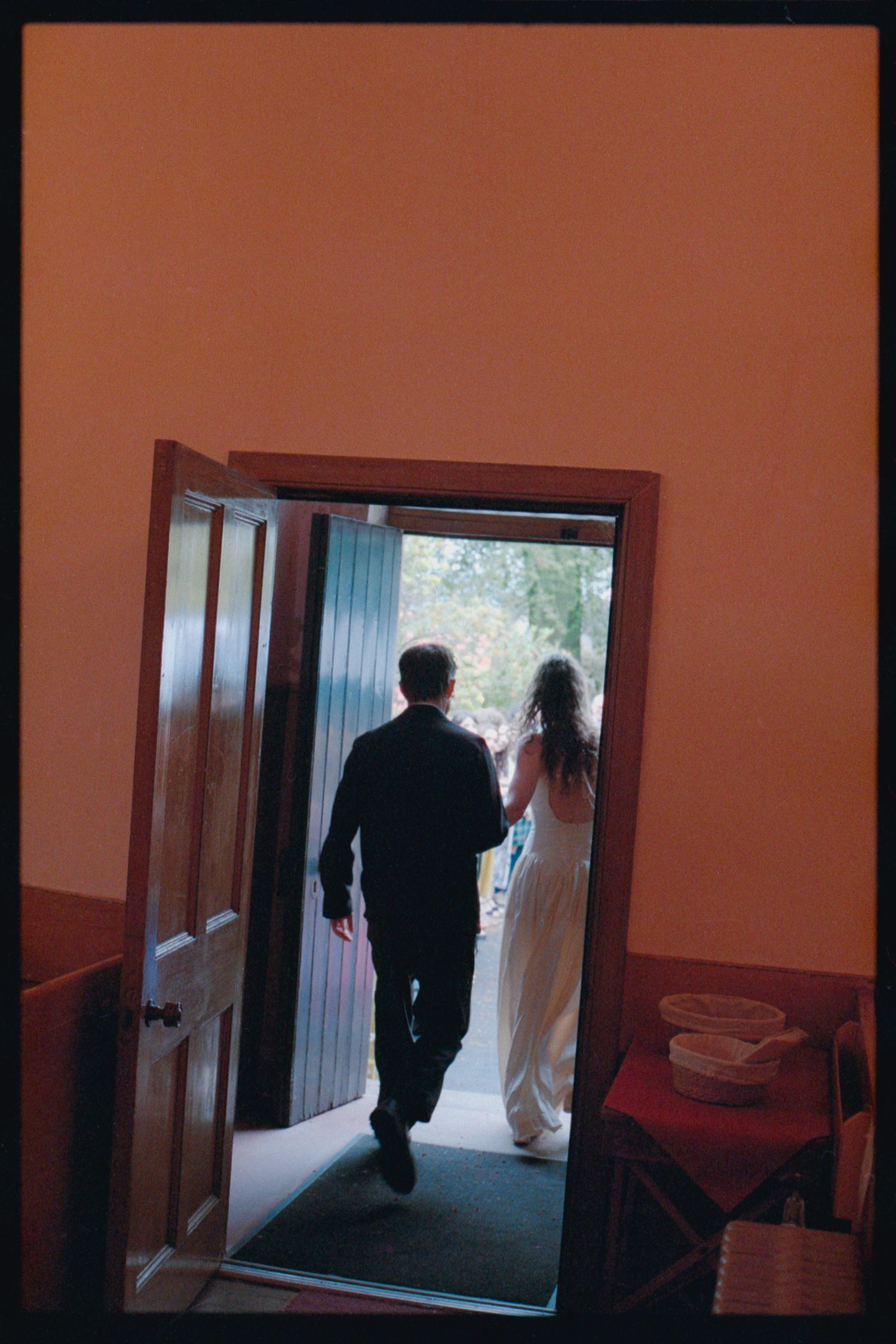 Bride and groom walking through doorway into light at wedding ceremony venue.