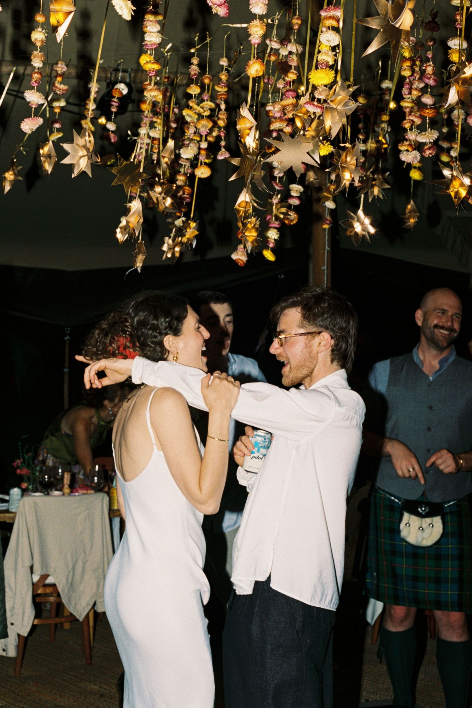 Bride and groom share a joyful first dance under floral hanging decorations at an outdoor wedding reception.