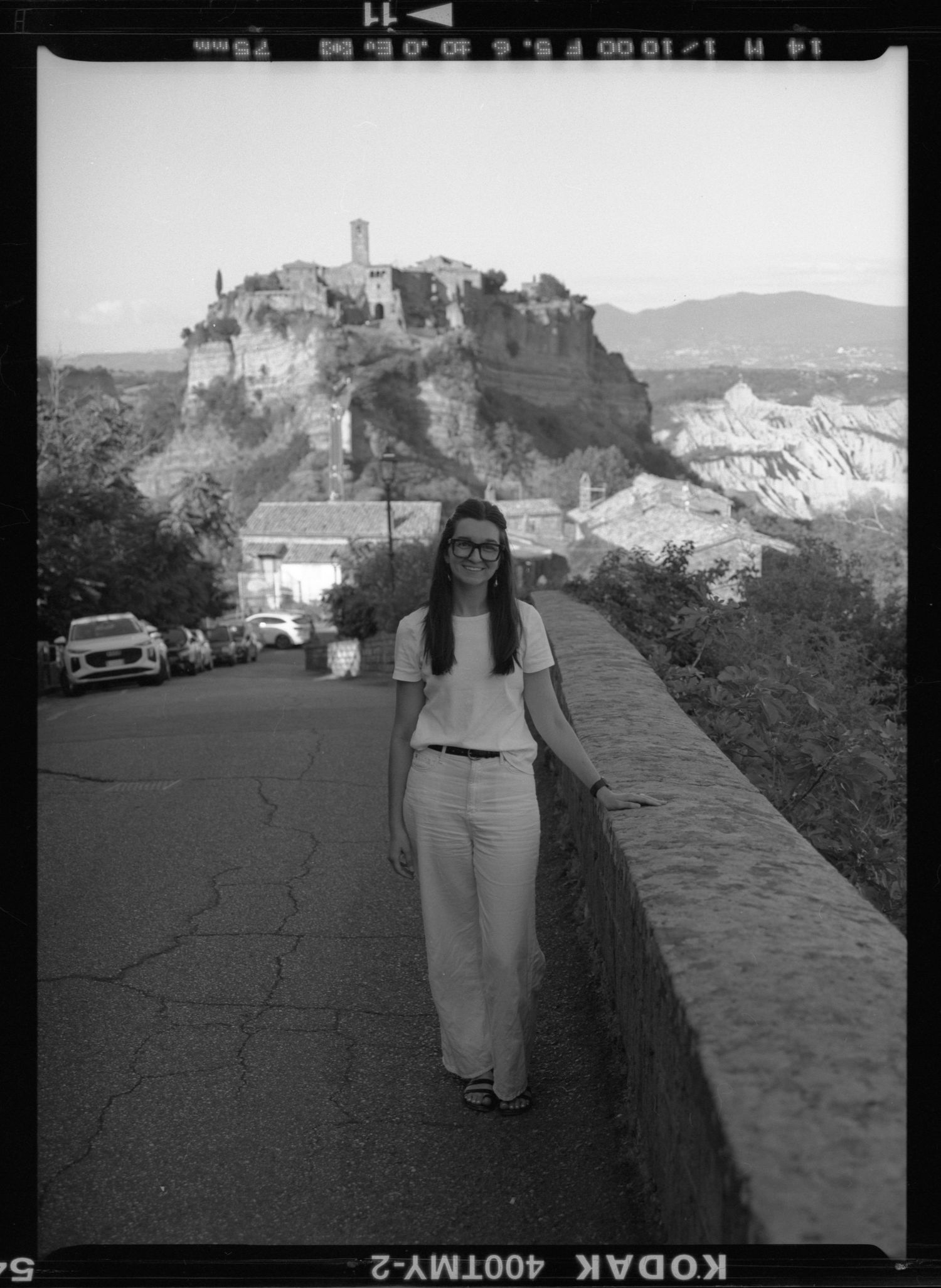 Woman walking on bridge path with ancient hilltop village of Civita di Bagnoregio in background.