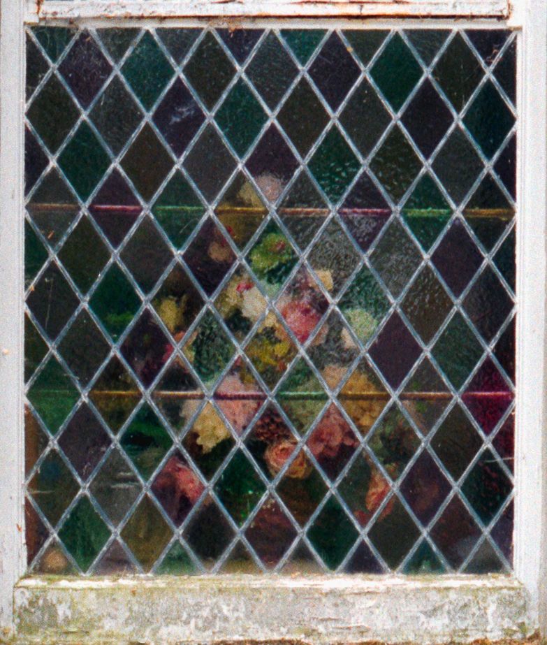 Colorful diamond-patterned leaded stained glass window with floral motifs in green, red, and yellow hues.