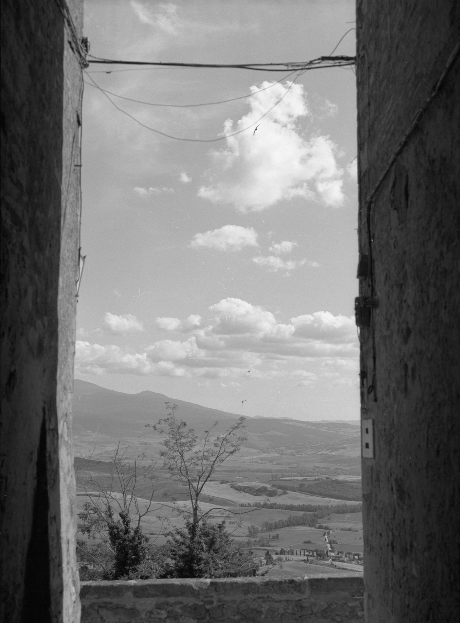 Black and white photo of a valley landscape framed by stone walls, with clouds and mountains in the background.