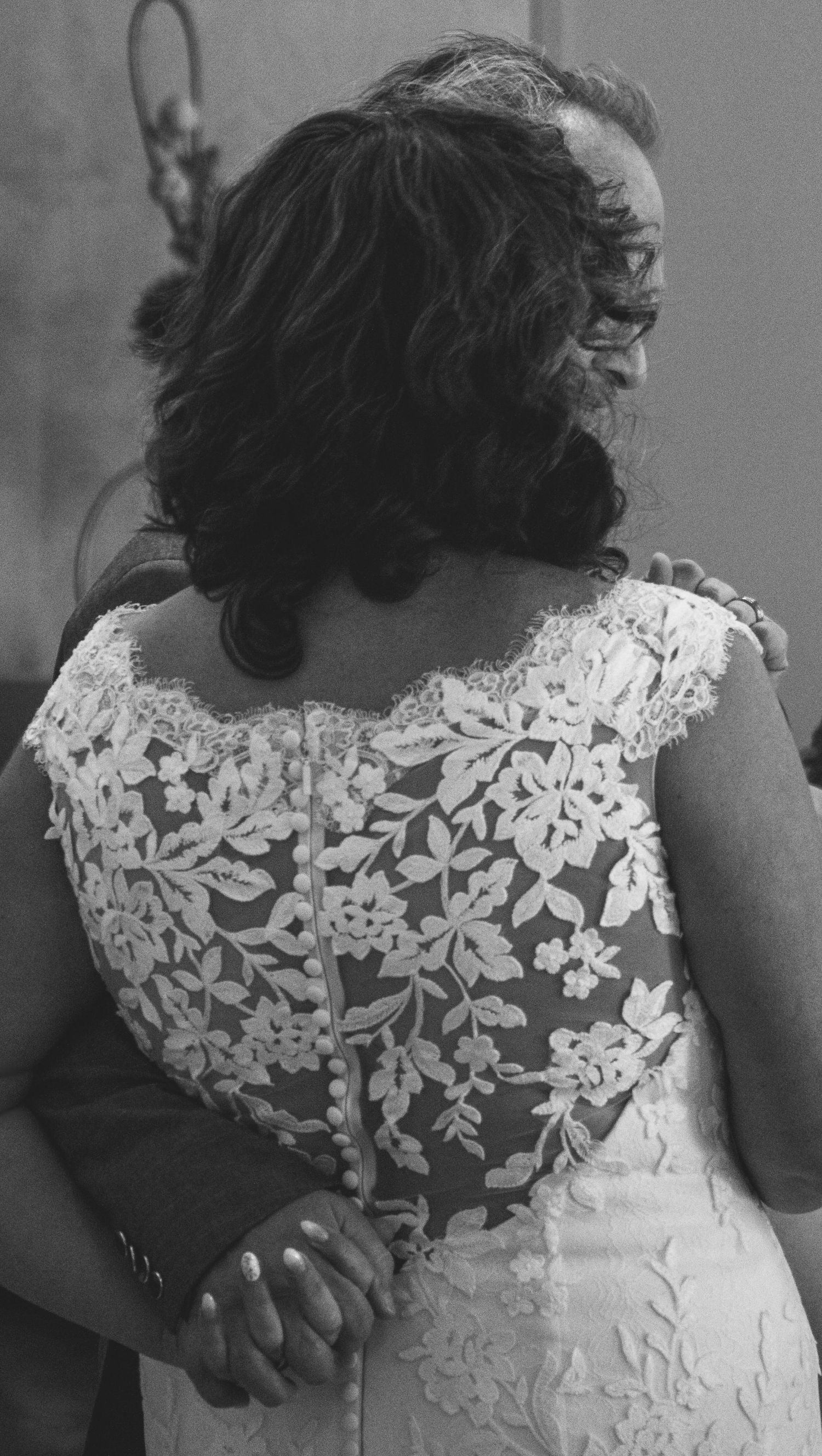 Black and white photo of a bride in lace wedding dress embracing someone from behind at a wedding ceremony.