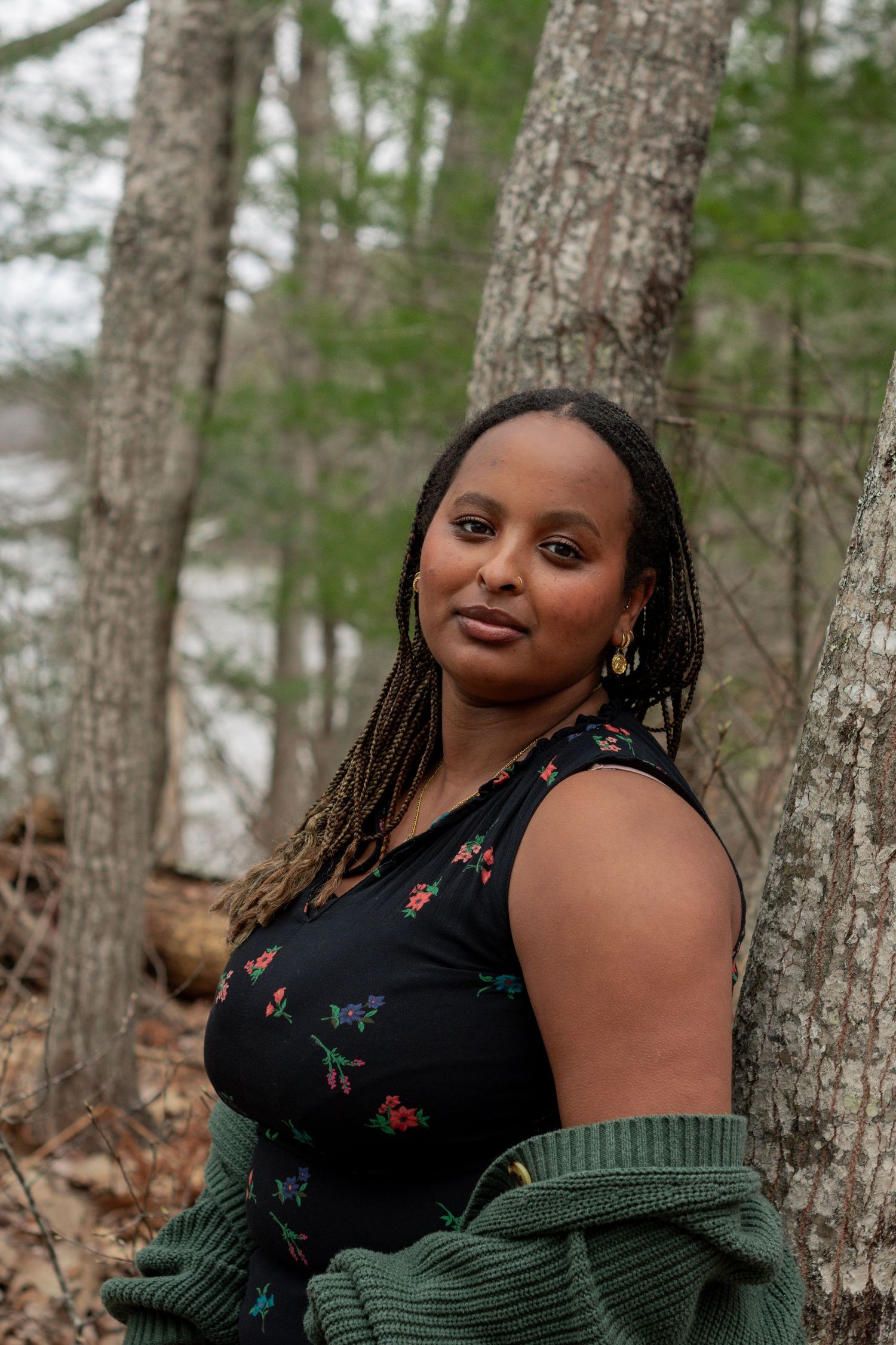 Woman in floral dress and green cardigan posing among trees in a forest setting.