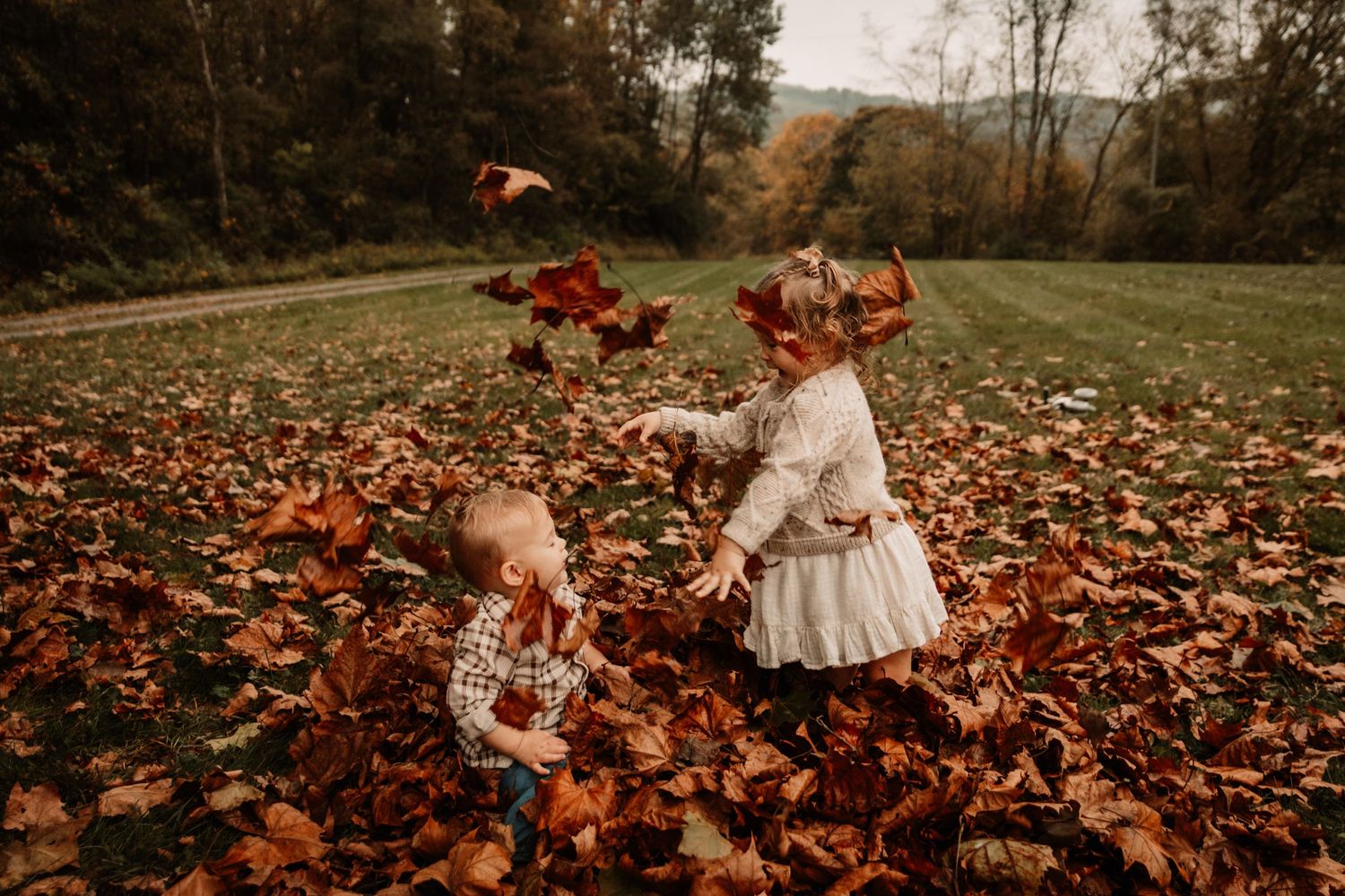 Children playing together in a field covered with vibrant orange and red autumn leaves on a crisp fall day.