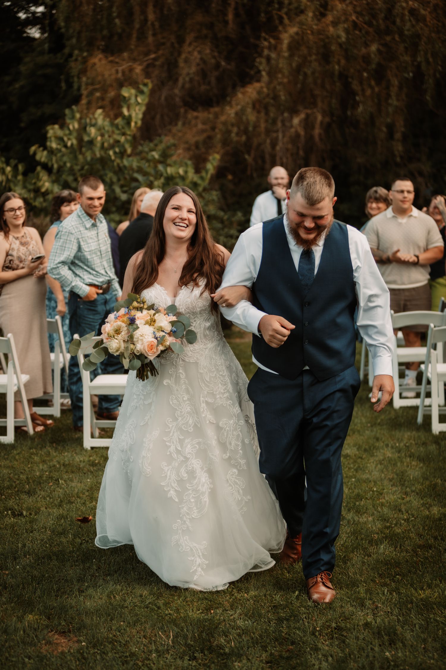 A couple walks down the outdoor aisle together while smiling and celebrating at their wedding ceremony.