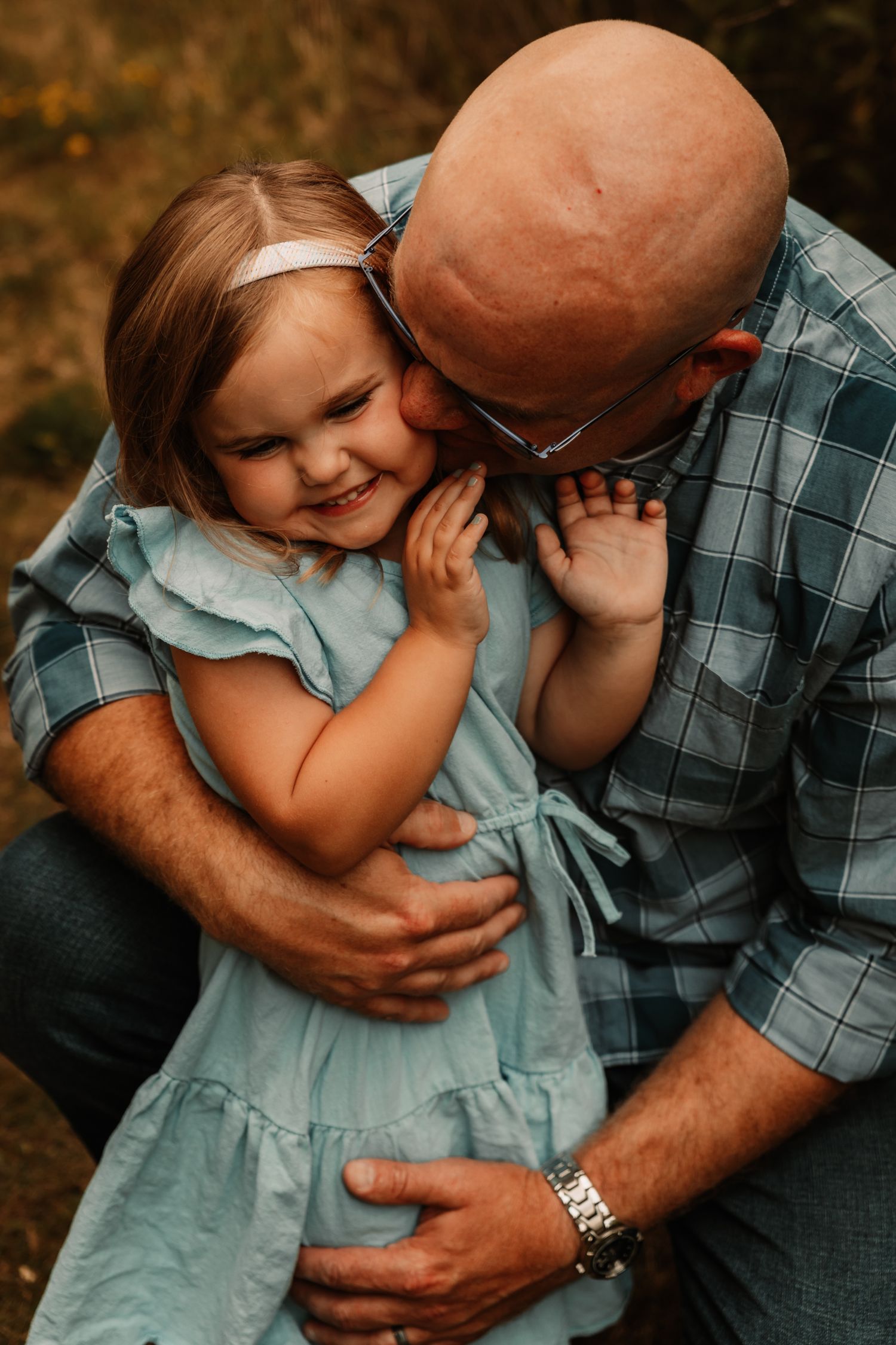 A heartwarming moment of laughter and affection captured between a parent and small child in a blue dress outdoors.