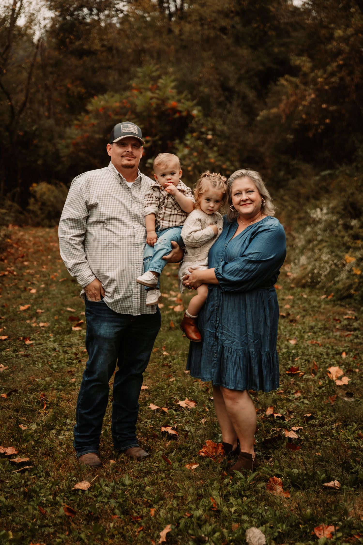 Group portrait in autumn setting with fallen leaves and wooded background, standing together outdoors.