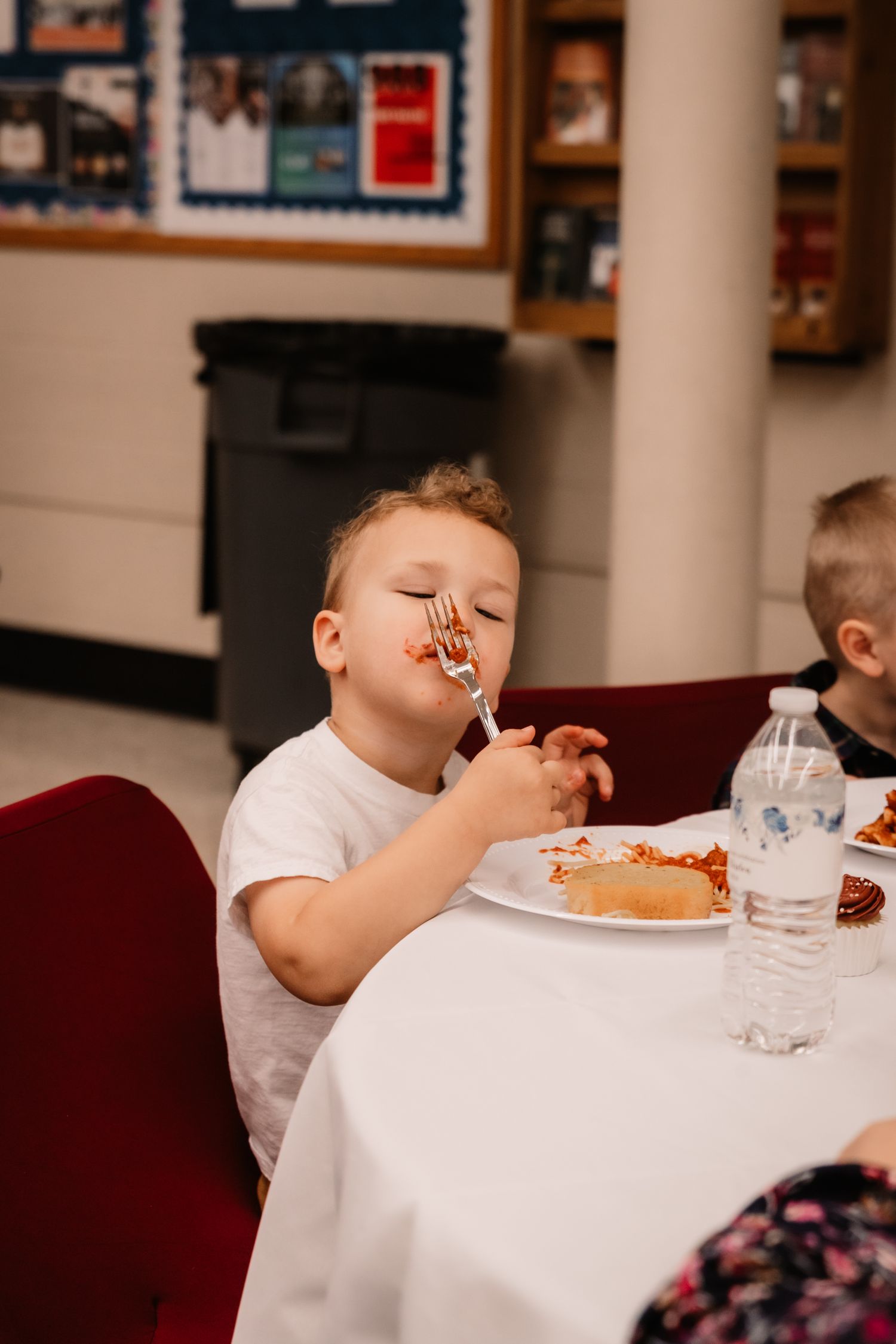 Young child enjoying messy spaghetti at a restaurant table with a white tablecloth.