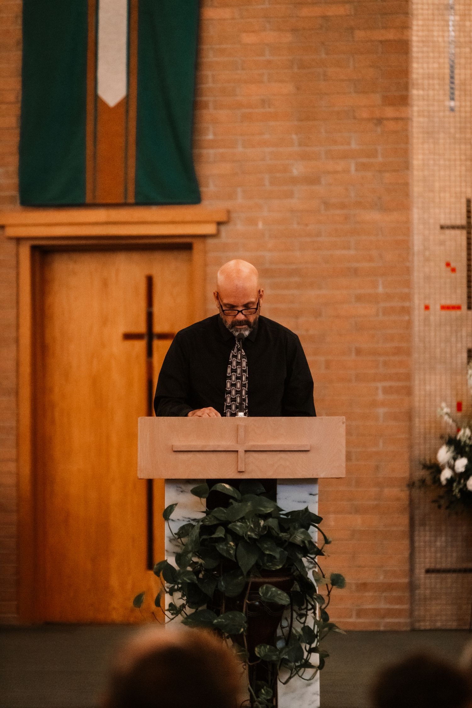 A speaker stands at an ornate wooden podium in a church with brick walls and a green banner hanging behind.