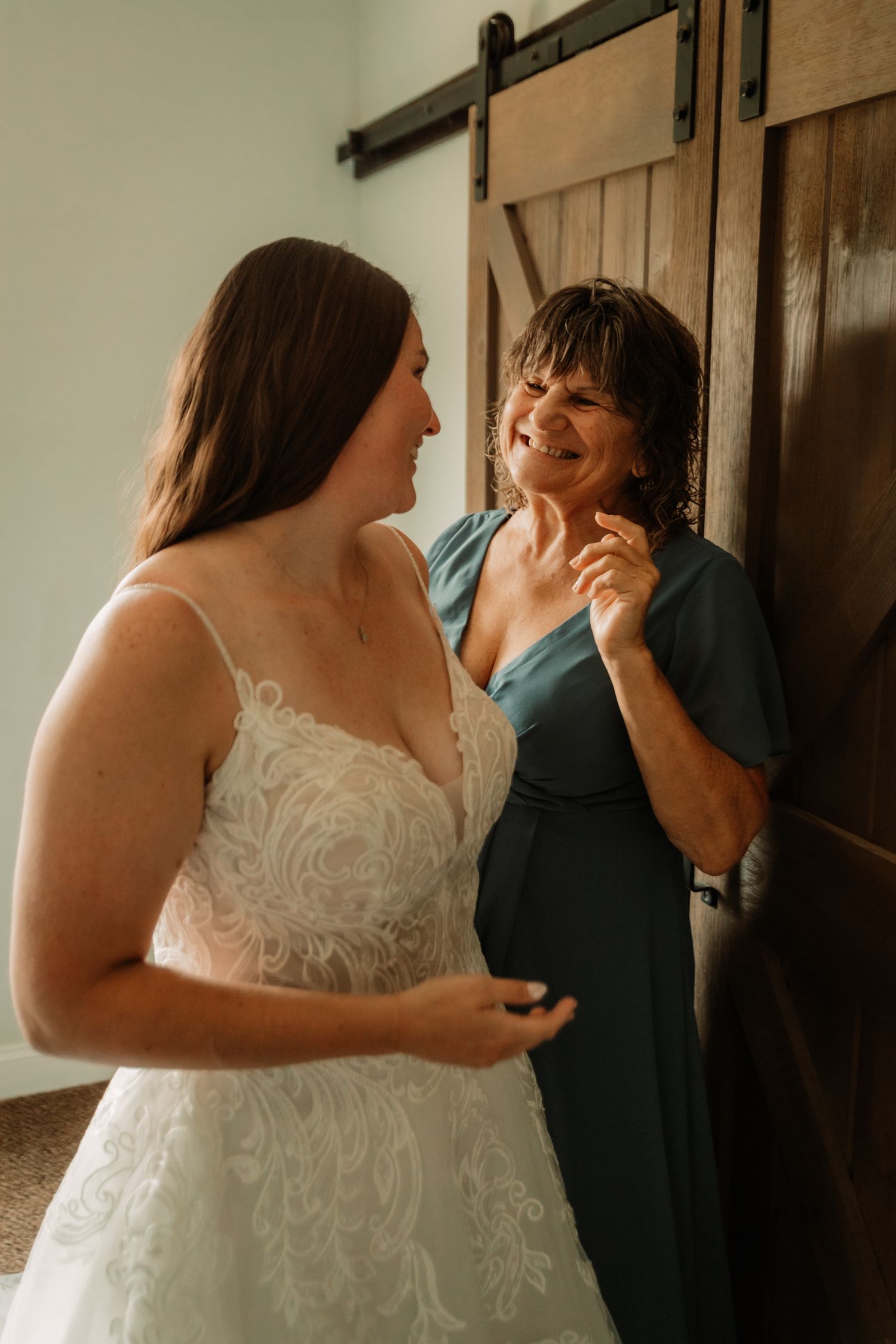 Two women sharing an emotional moment together, one in a white lace wedding dress and another in a teal dress.