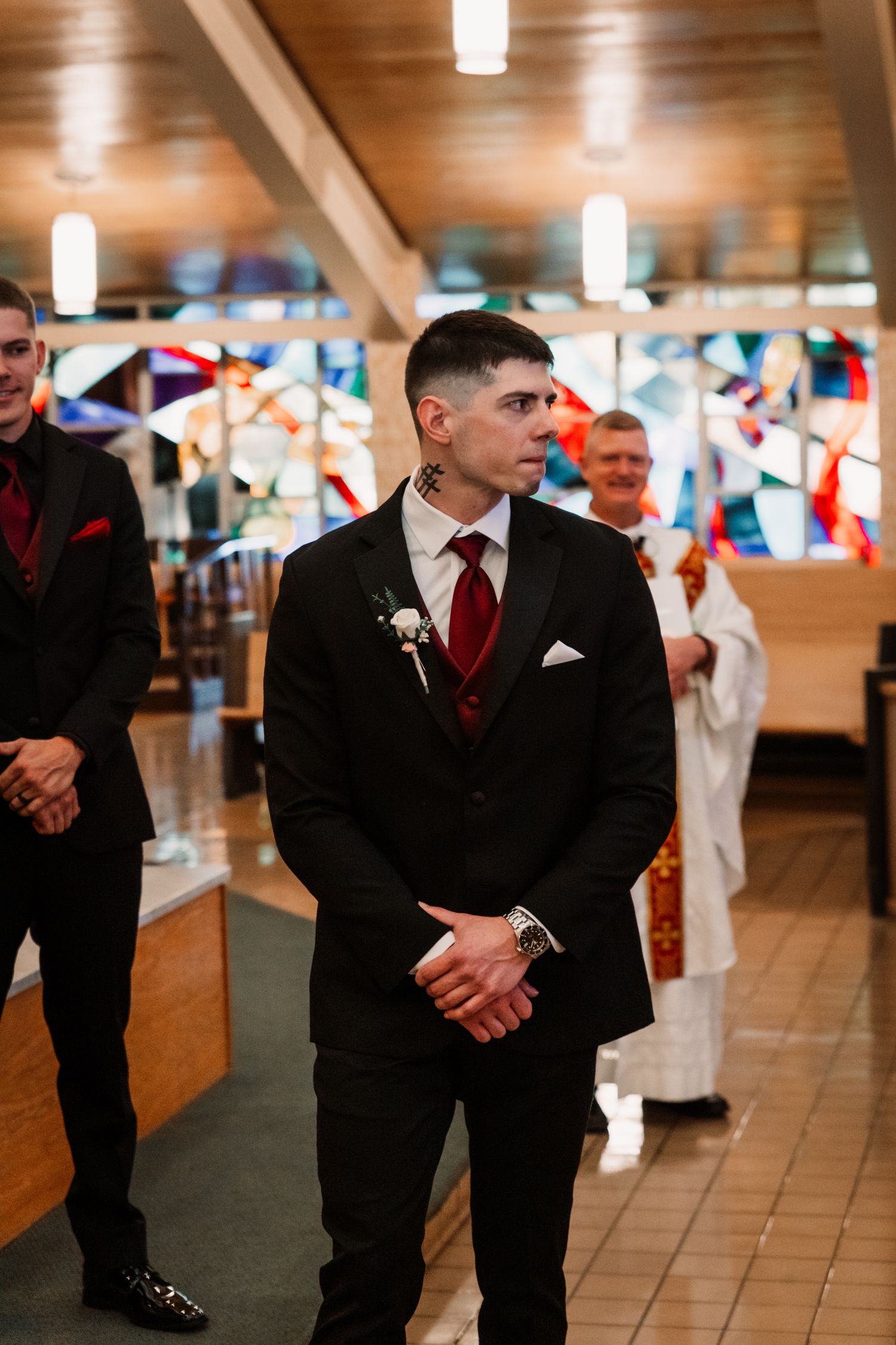 Wedding attendee in black suit with red tie standing in church hallway decorated with colorful bunting flags.
