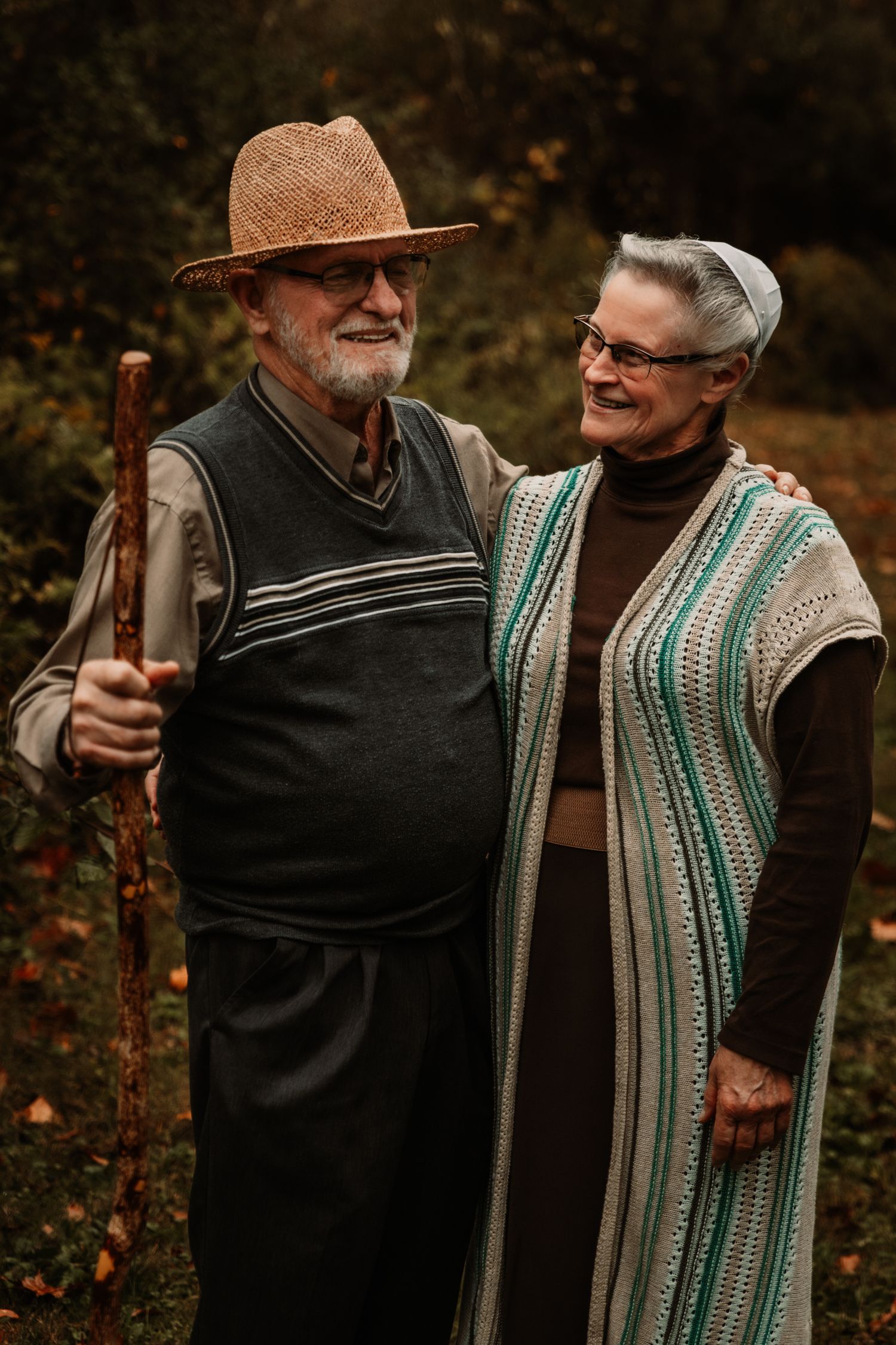 Senior couple wearing autumn sweaters and cozy knitwear share a warm moment outdoors with walking stick.