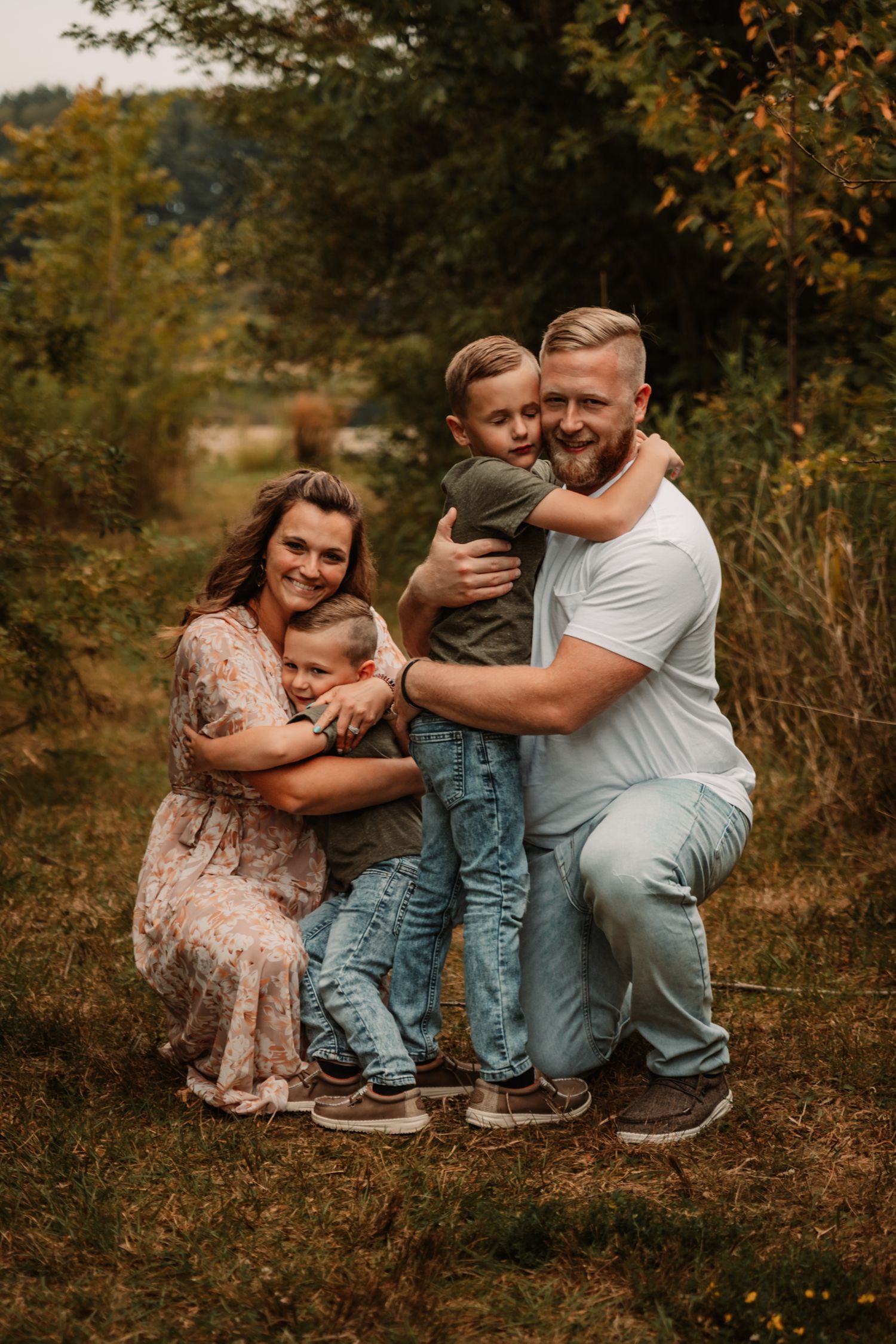 A family poses together on an autumn path surrounded by fall foliage and warm golden light.