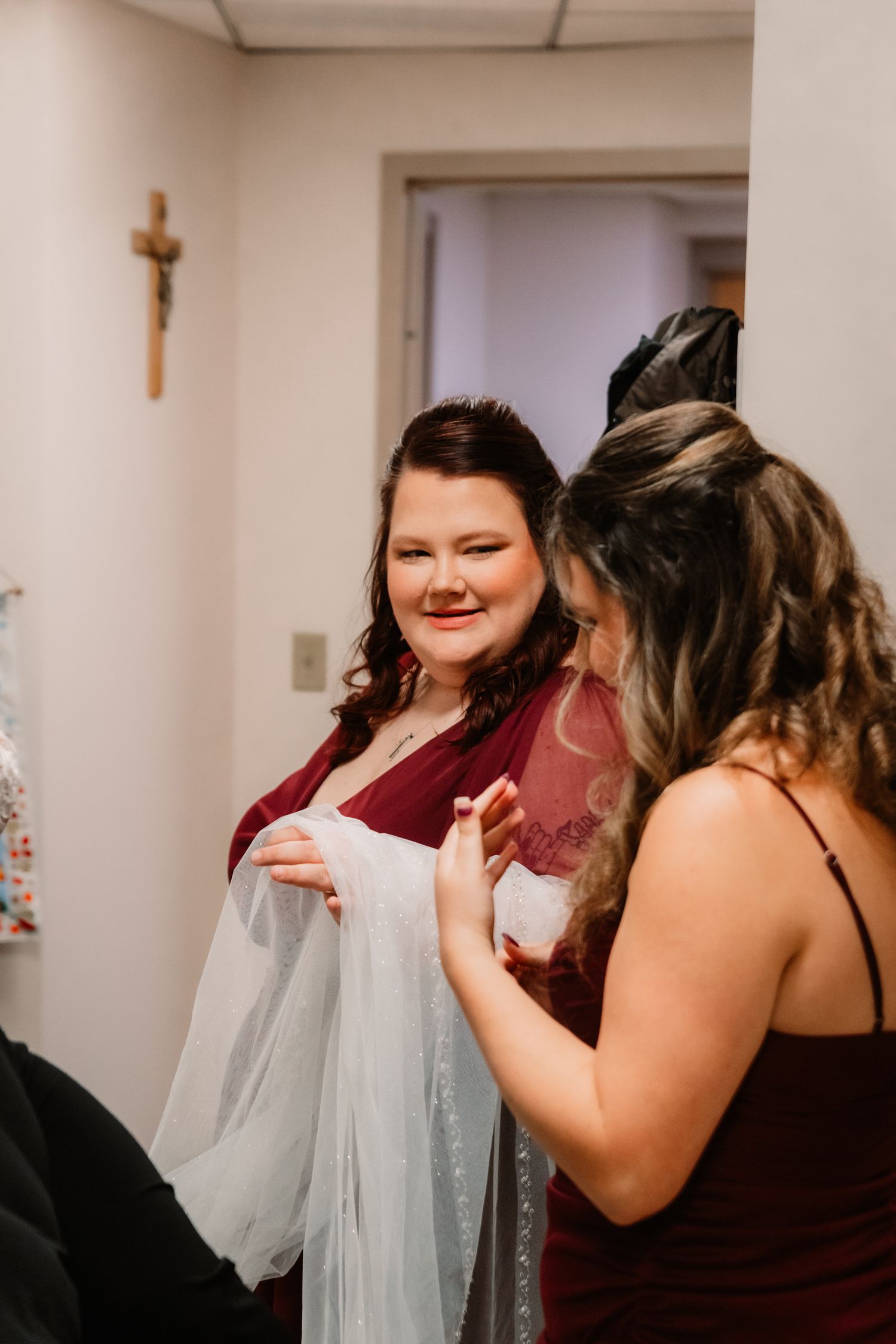 Wedding preparations in a room with burgundy bridesmaids dresses and a crucifix on the wall.