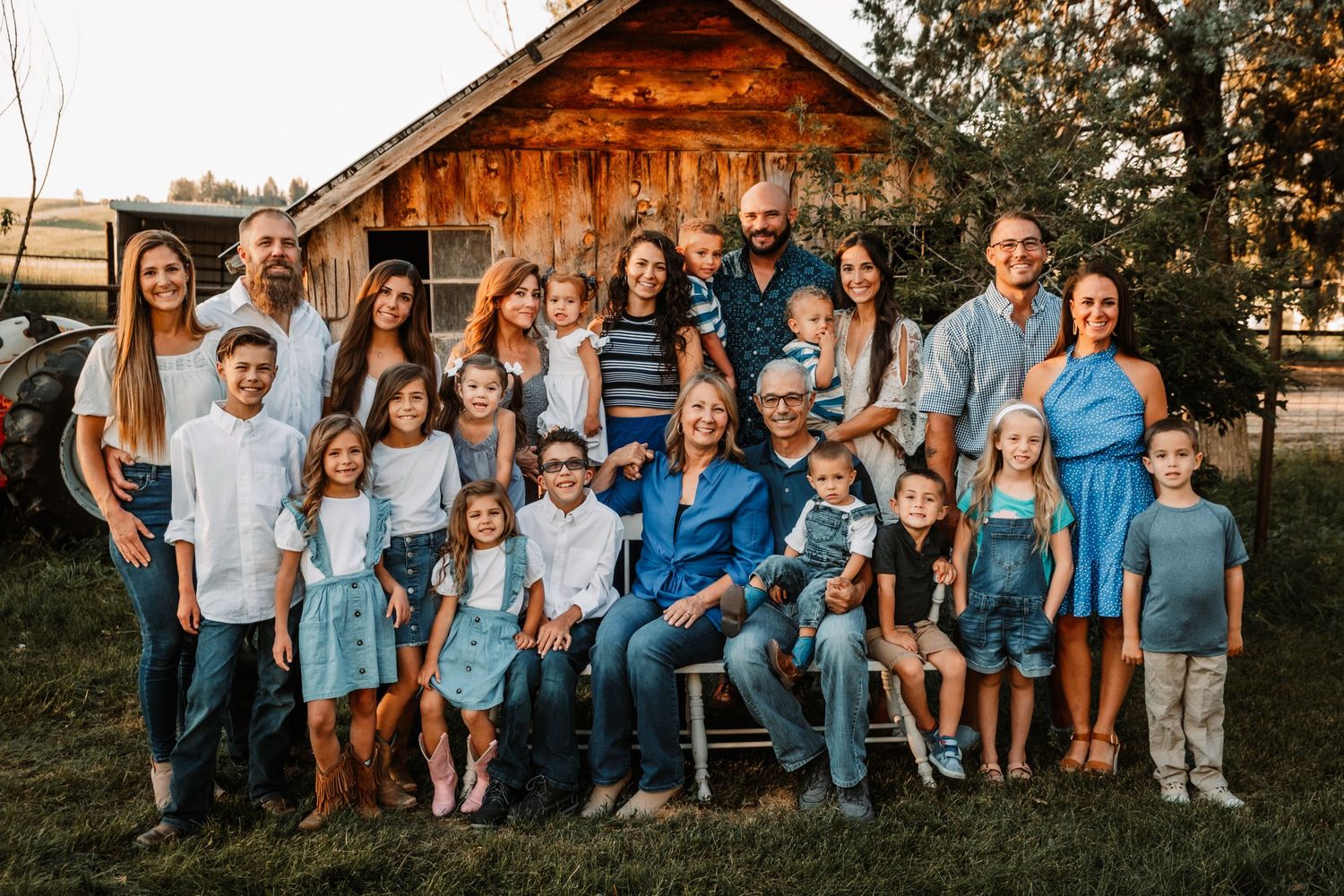 A large group wearing coordinated blue and white outfits poses together in front of a rustic wooden cabin at sunset.