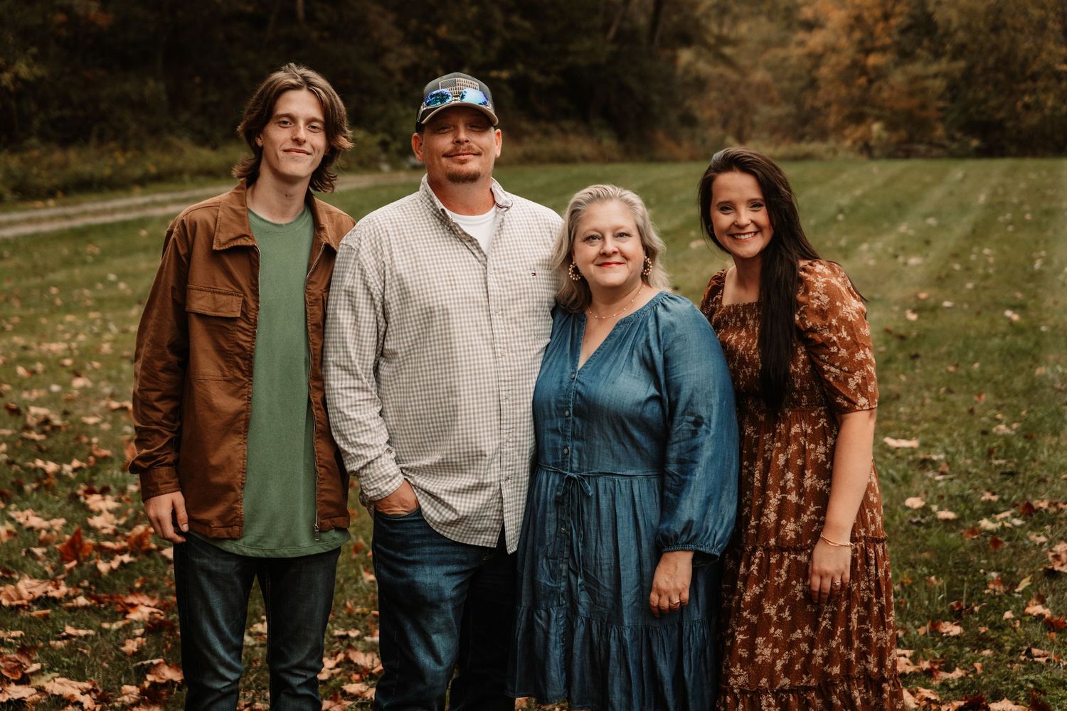 A family of four poses together outdoors in fall, with autumn leaves scattered on the ground around them.