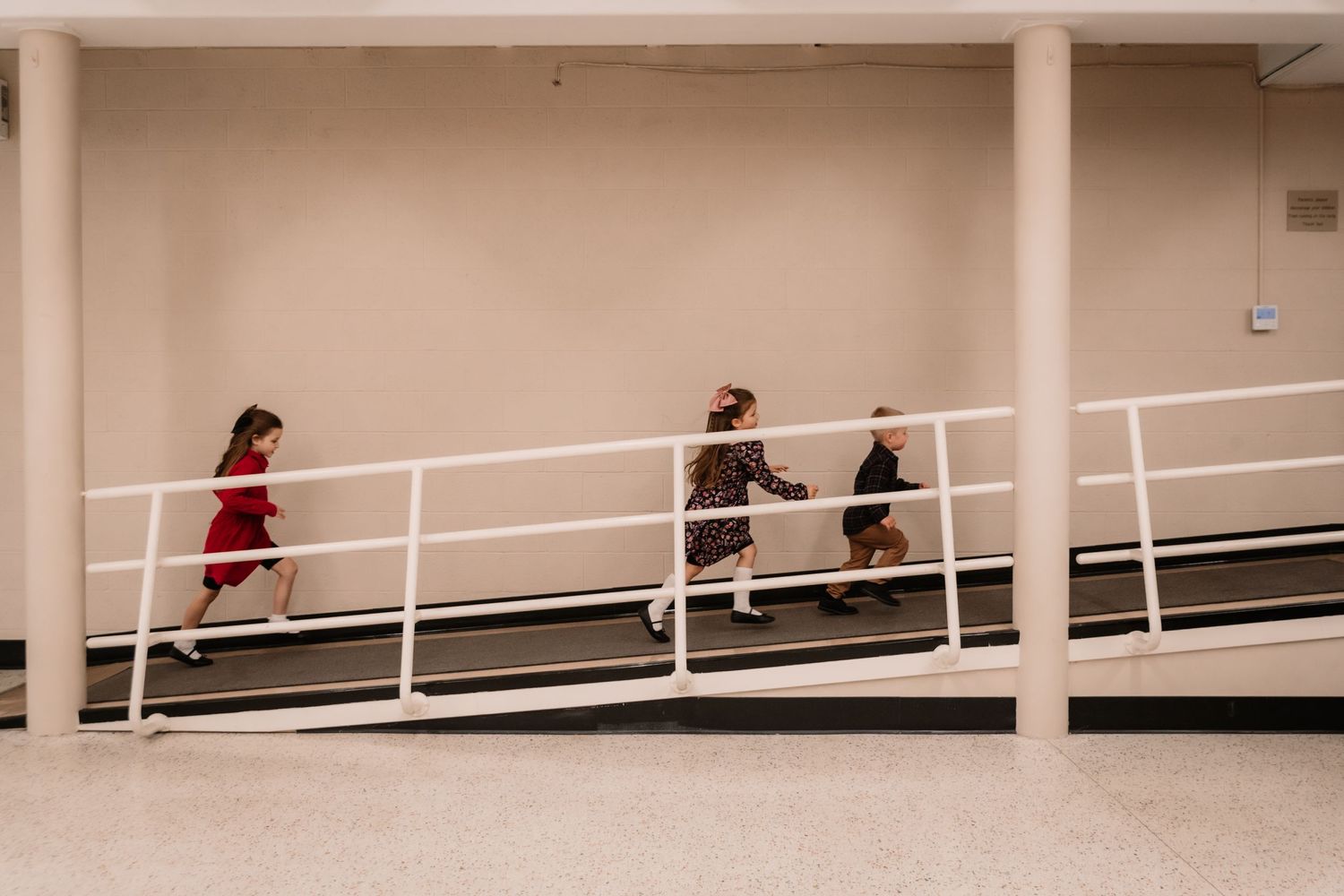 People walk up a sloped, beige hallway with white handrails on both sides.