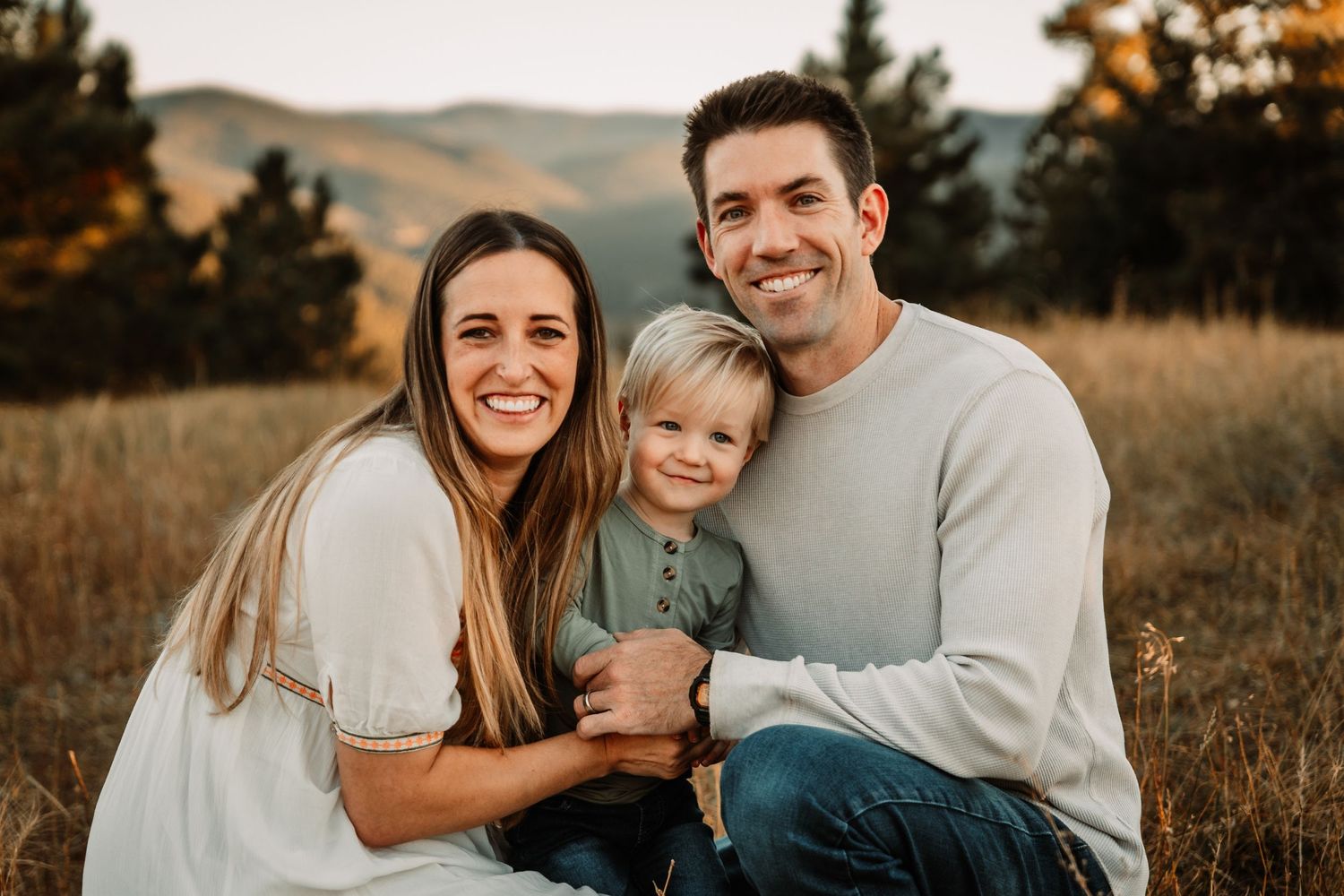 A family shares a tender moment during their outdoor portrait session in a mountain field.