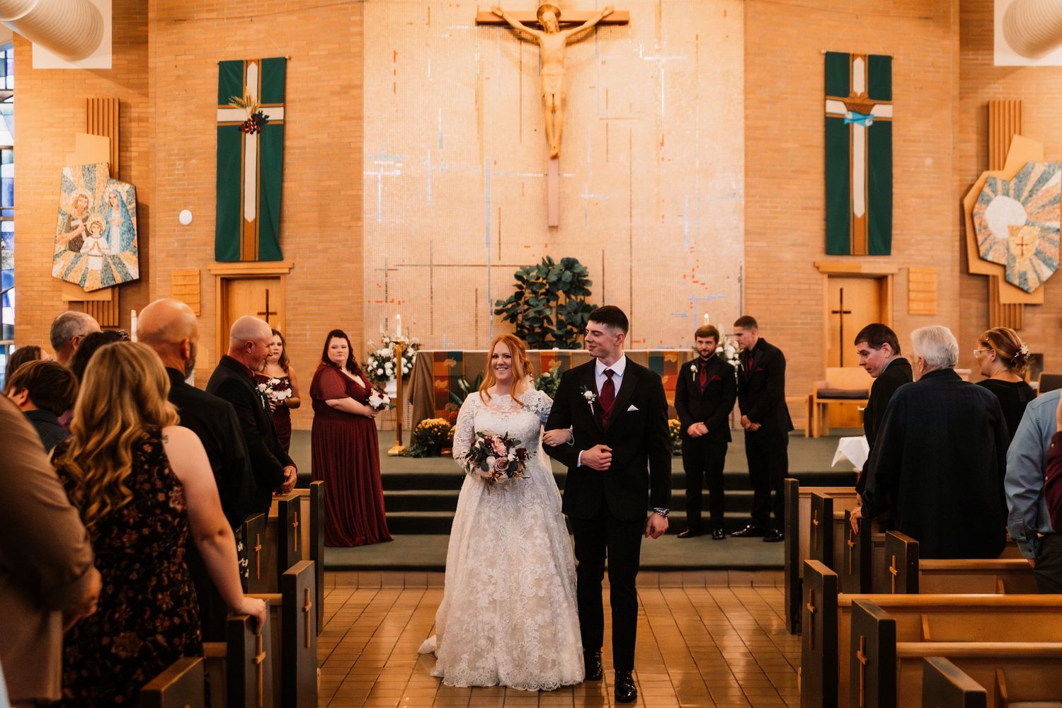 A wedding couple walks down the aisle in a traditional church ceremony with stained glass windows and crosses.