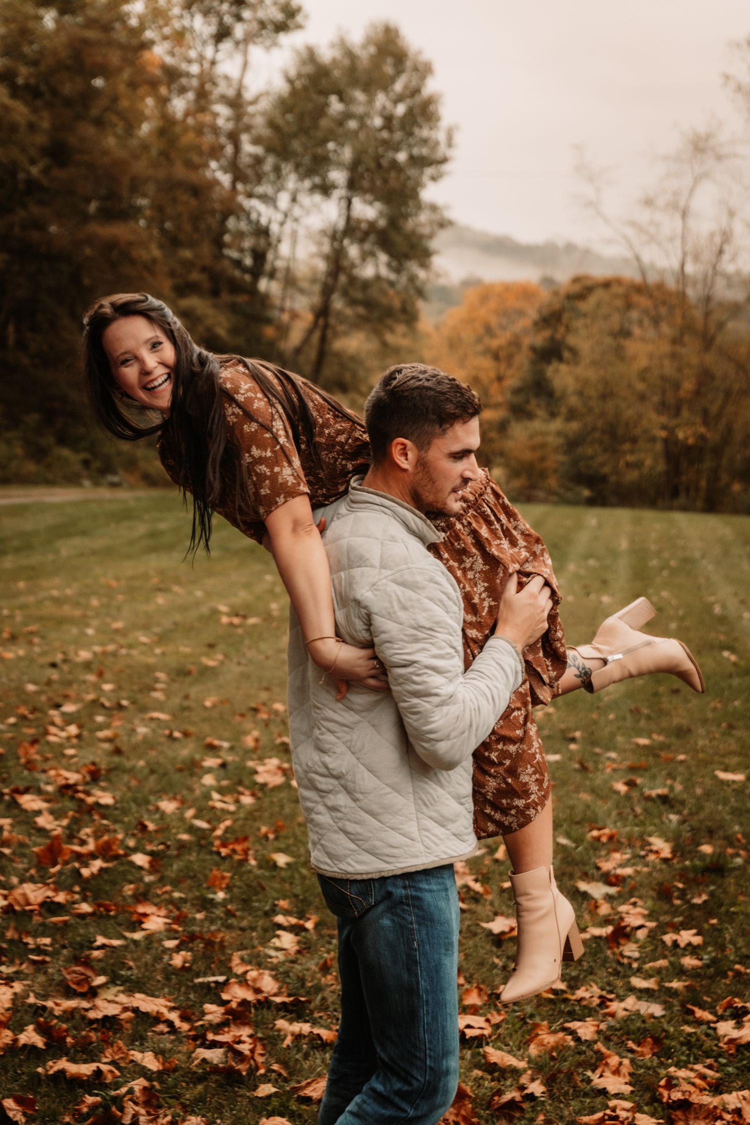 A playful fall photography session captures a couple having fun in the woods with autumn foliage all around.