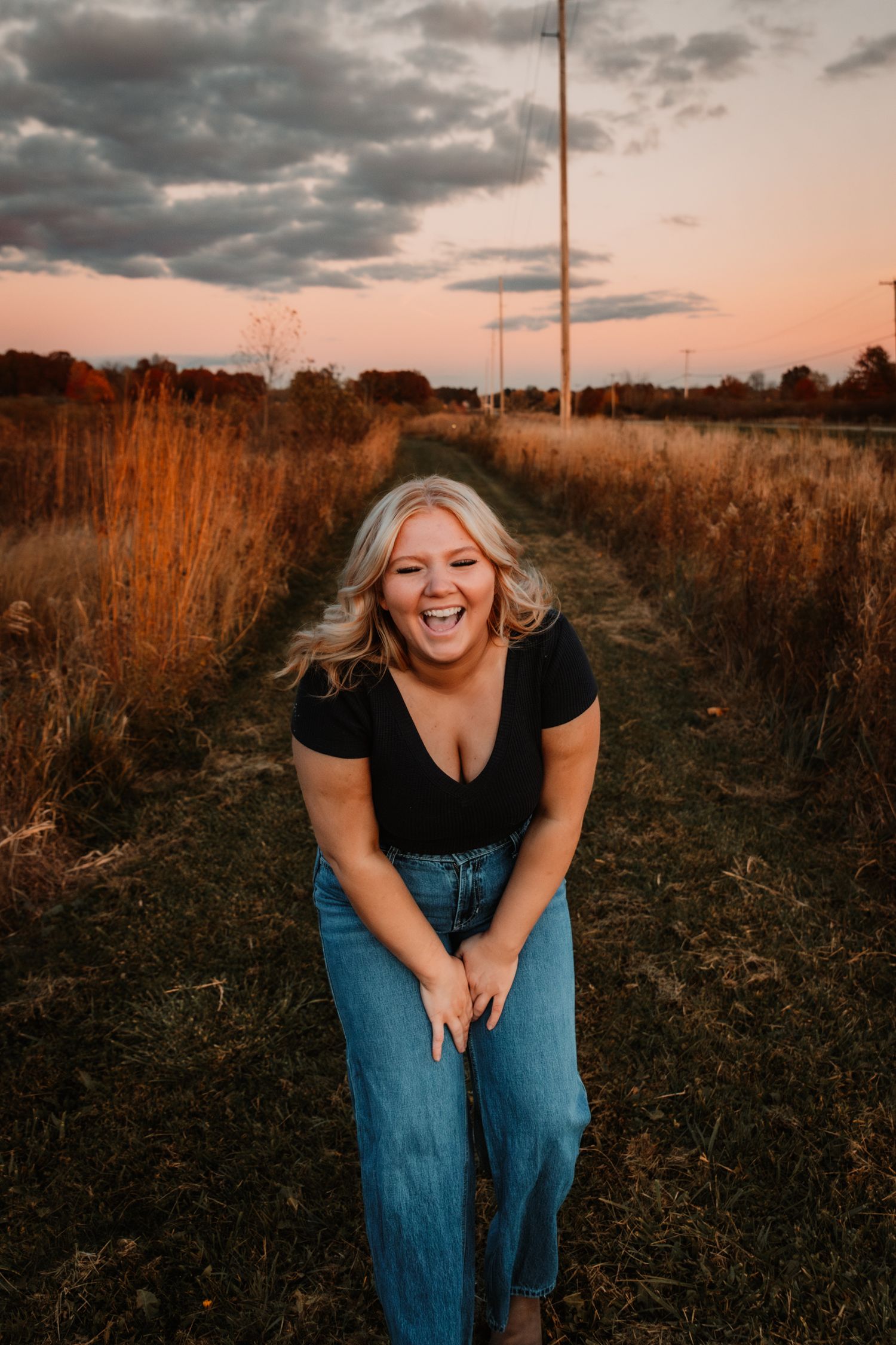A joyful moment captured during golden hour in a rural field with tall grass and moody sunset clouds in the background.