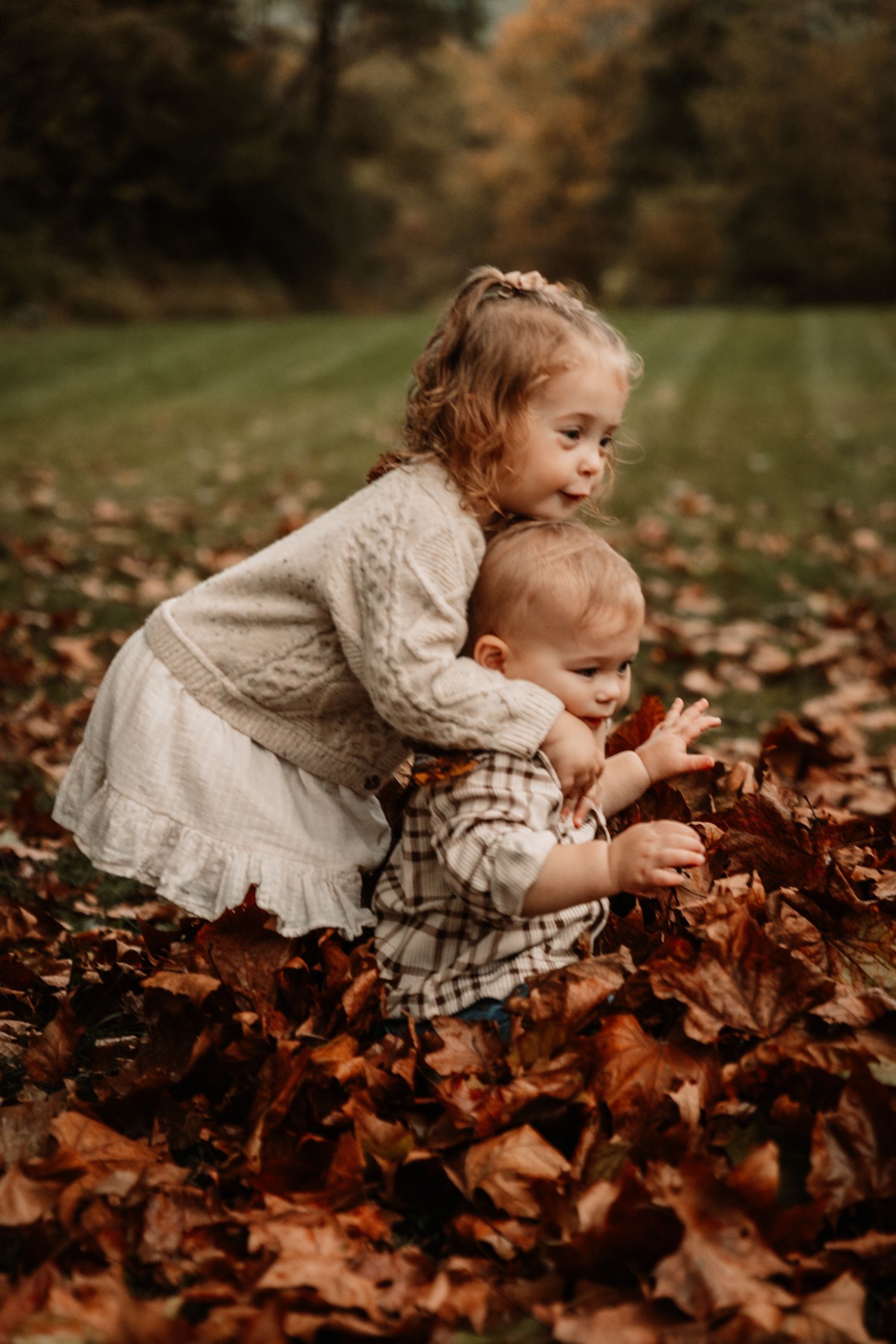 Two small children playing together in a pile of fallen autumn leaves on a crisp fall day.