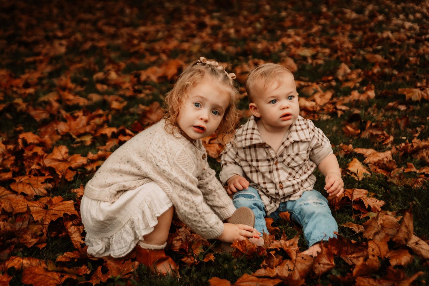 Two young children play together in a carpet of colorful autumn leaves.