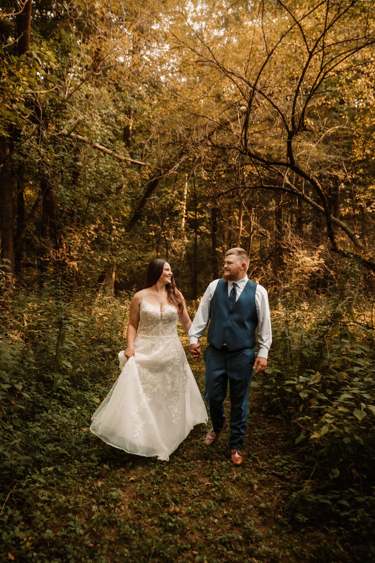 A couple walks hand in hand through a golden autumn forest on their wedding day.