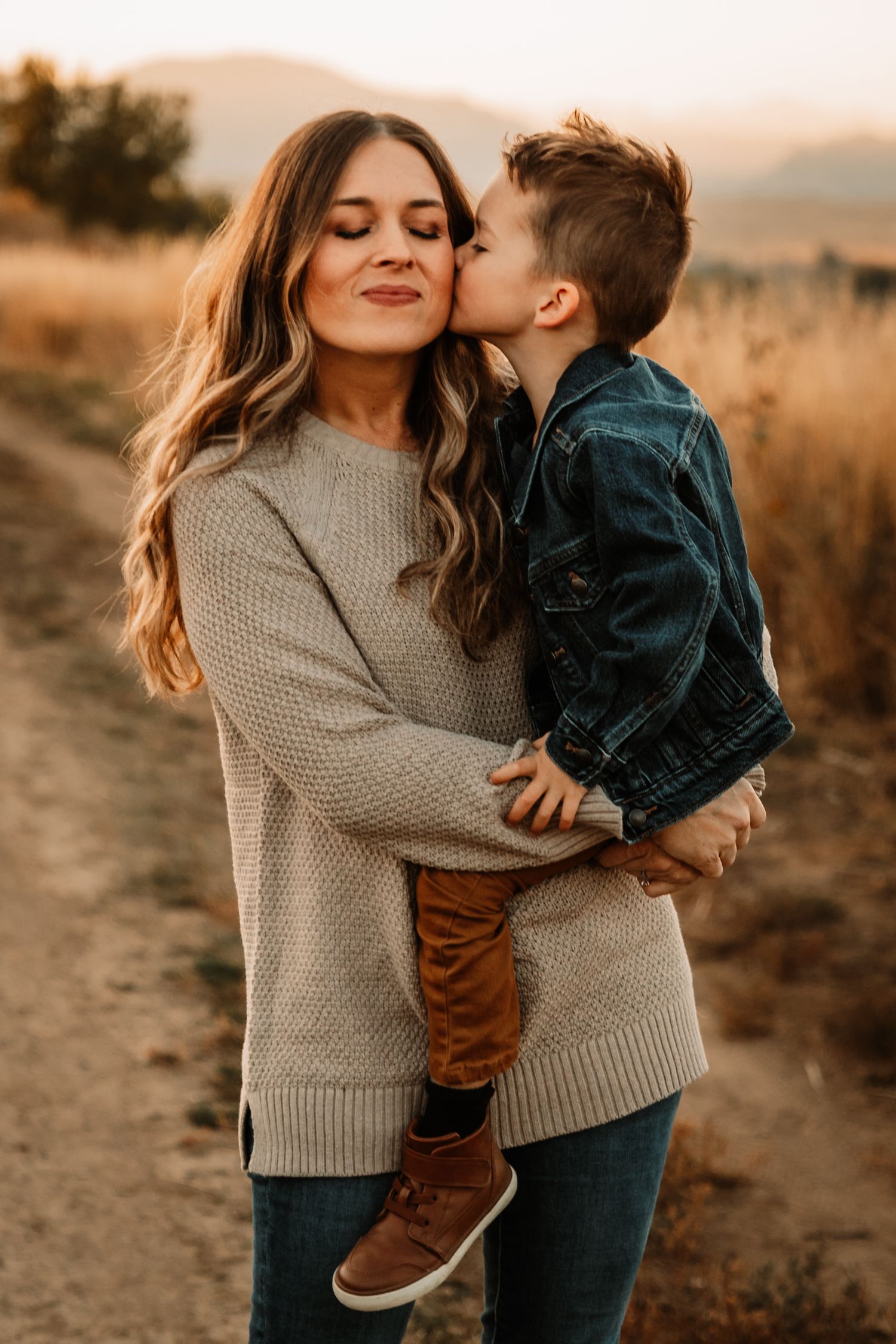 A tender moment between parent and child sharing a kiss at sunset on a dirt path in golden autumn light.