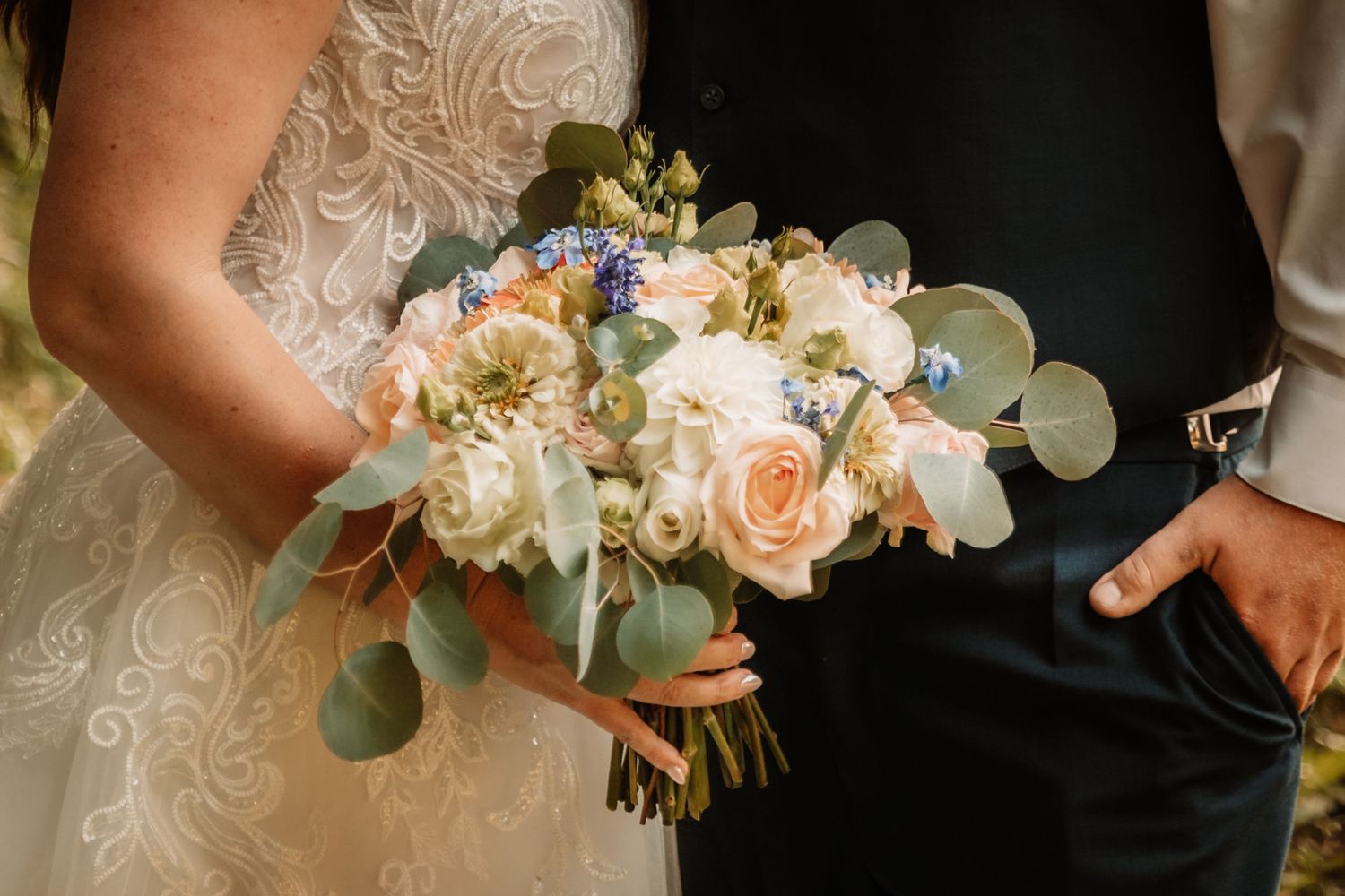 Close-up of elegant bridal bouquet with peach roses, white flowers and eucalyptus leaves held between formal attire.