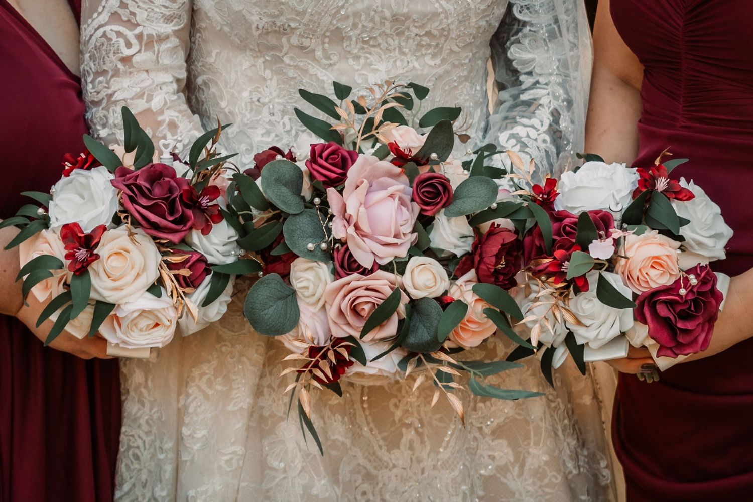 Three wedding bouquets featuring burgundy and blush roses with eucalyptus greenery against lace dress detail.