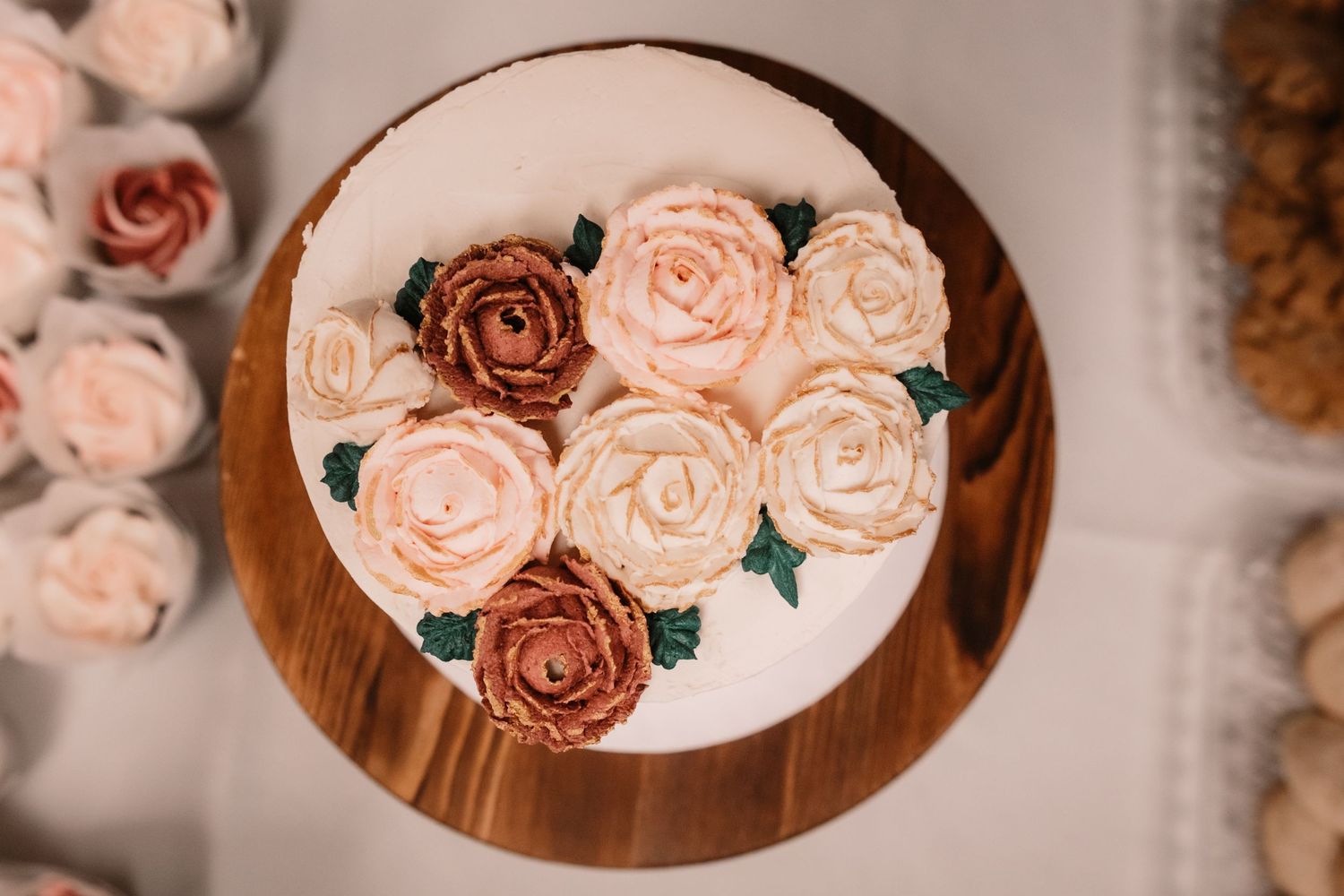 Overhead view of buttercream roses in pink and brown tones arranged on a round wooden board.