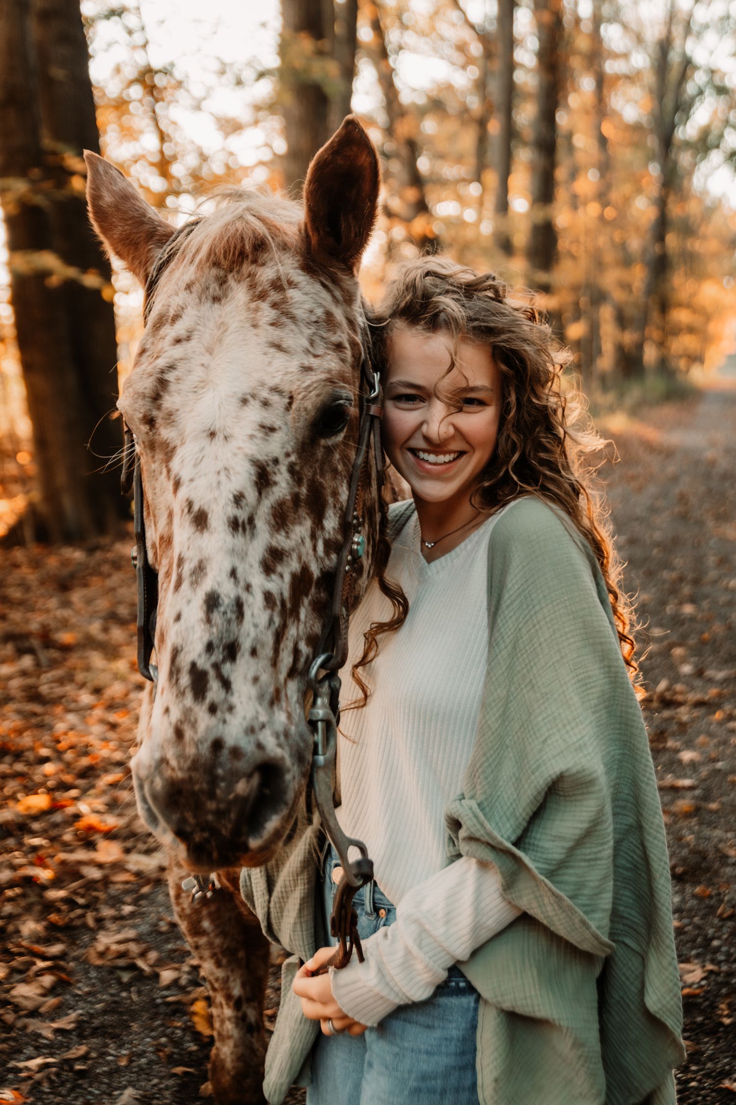 A spotted white horse and person in a green sweater share a joyful moment in an autumn forest setting.